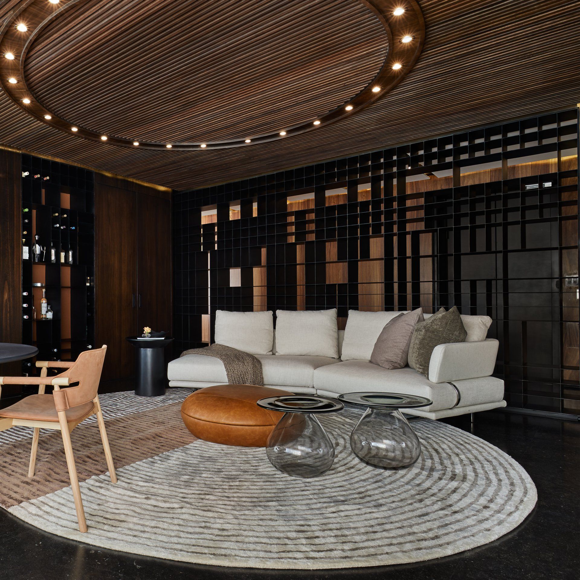 Salón moderno con sofá curvo, alfombra redonda, mesas de cristal y decoración cálida en madera y negro.
