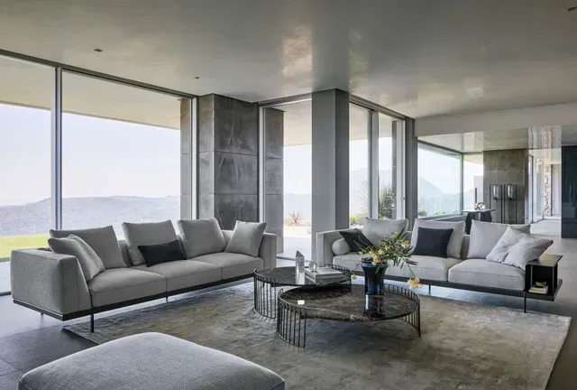 Sala de estar moderna con sofás grises, paredes de cristal y una mesa de centro con vistas panorámicas.