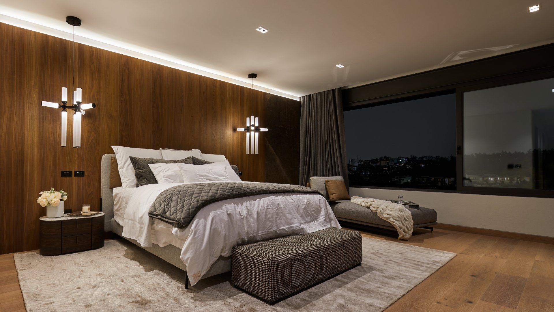 Dormitorio moderno con pared revestida de madera, cama grande, bancos y ventanales que van del suelo al techo
