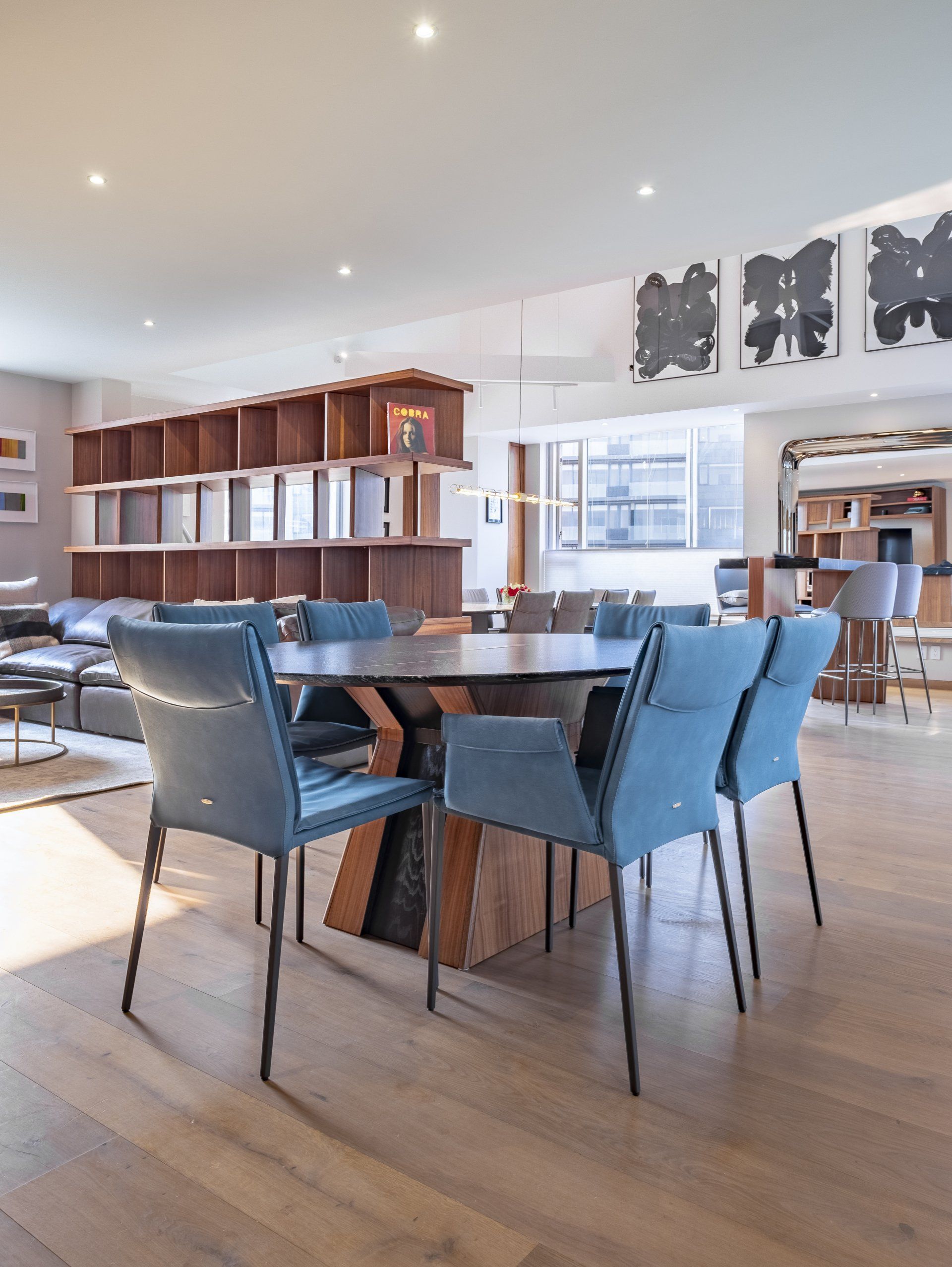 Comedor moderno con mesa de madera, sillas azules y armarios empotrados cerca de grandes ventanales.