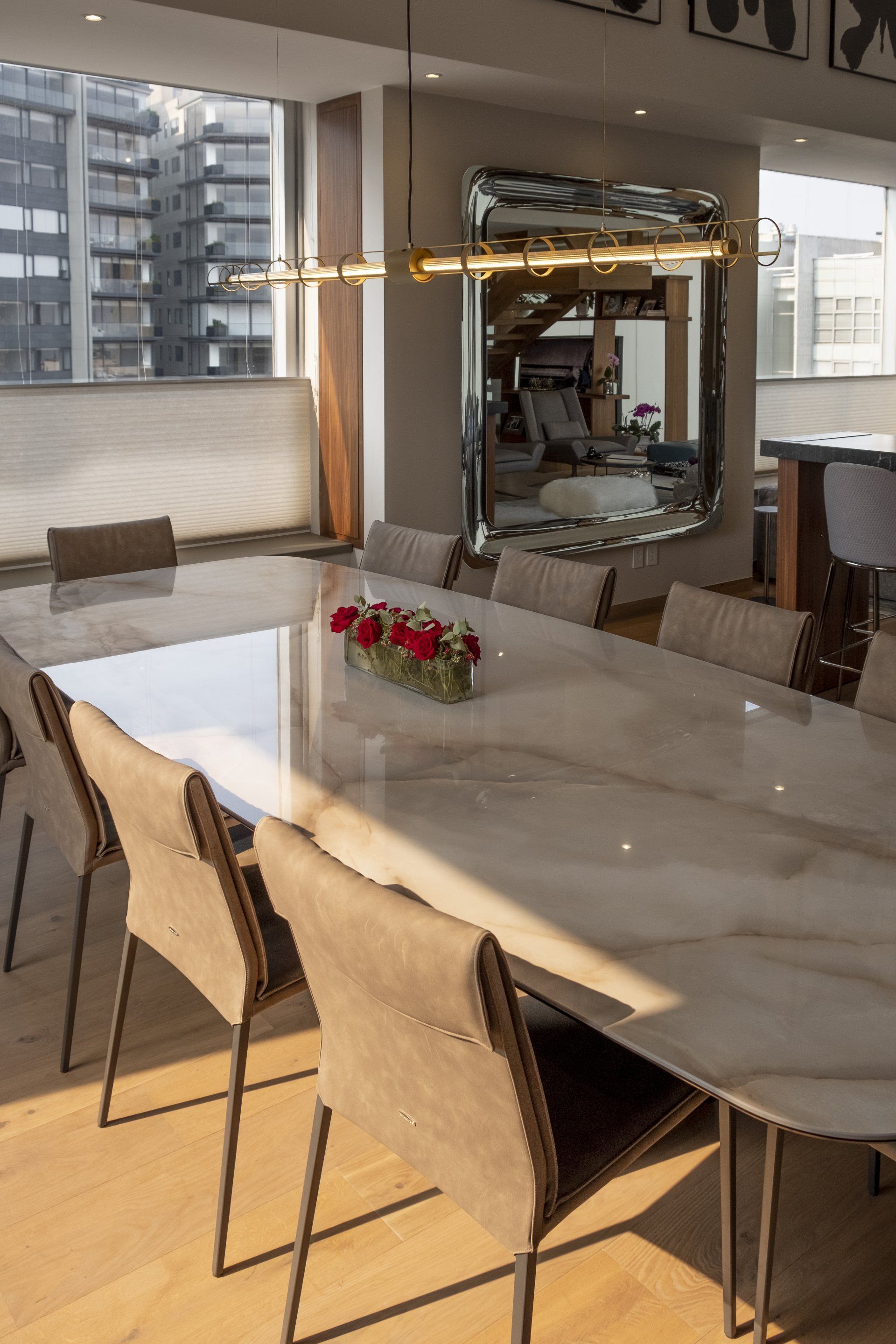 Comedor moderno con mesa de mármol, sillas de mimbre y ventanas con vistas a la ciudad.