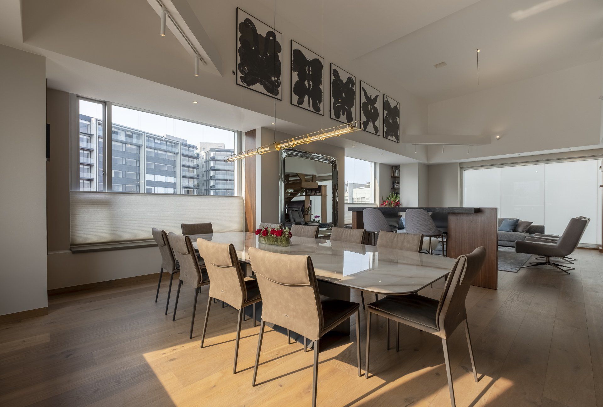 Salón-comedor moderno de concepto abierto con grandes ventanales, suelos de madera y muebles en tonos neutros.