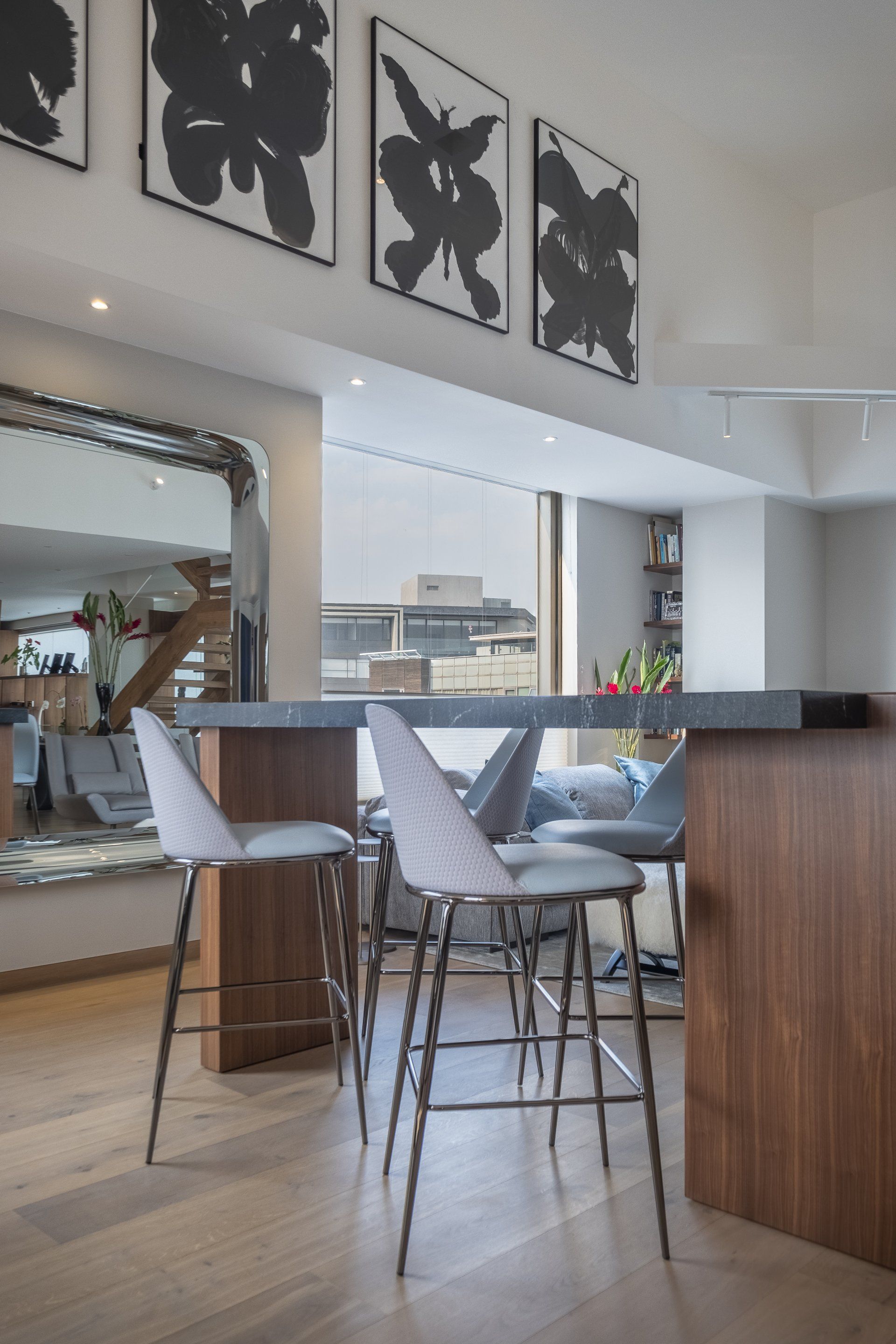 Barra de cocina moderna con taburetes blancos, armarios de madera y un cuadro en blanco y negro en la pared superior.