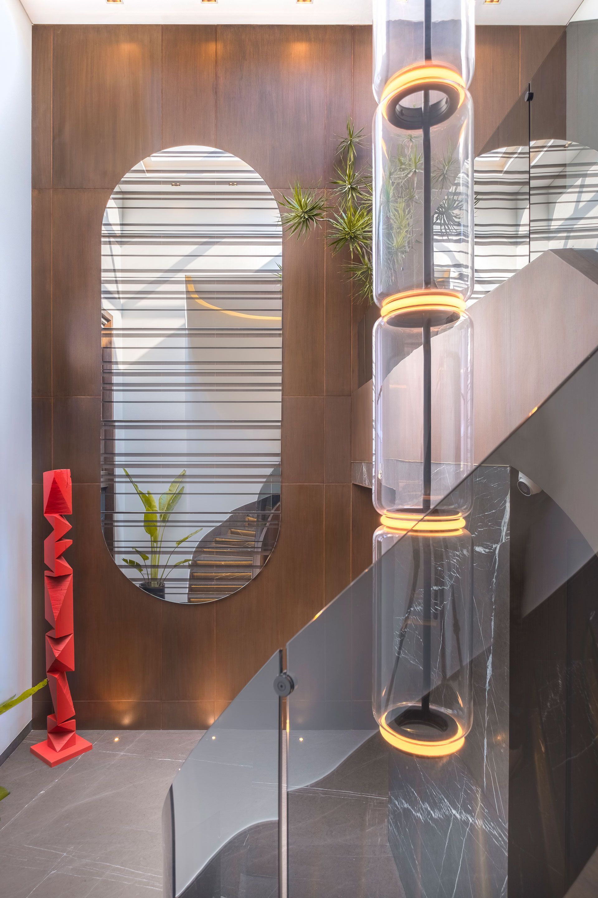 Interior moderno con lámparas circulares colgantes, escalera y pared decorativa de madera con espejo ovalado.
