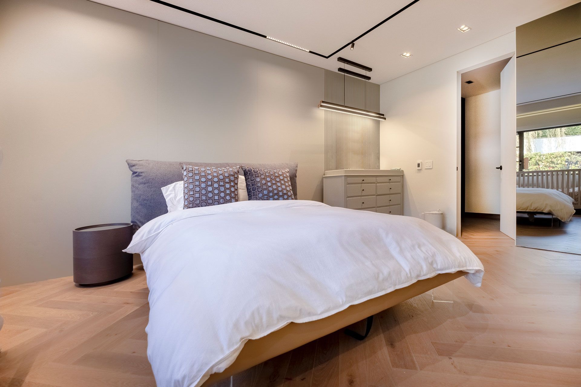 Dormitorio moderno minimalista con cama, cómoda y suelos de madera clara.