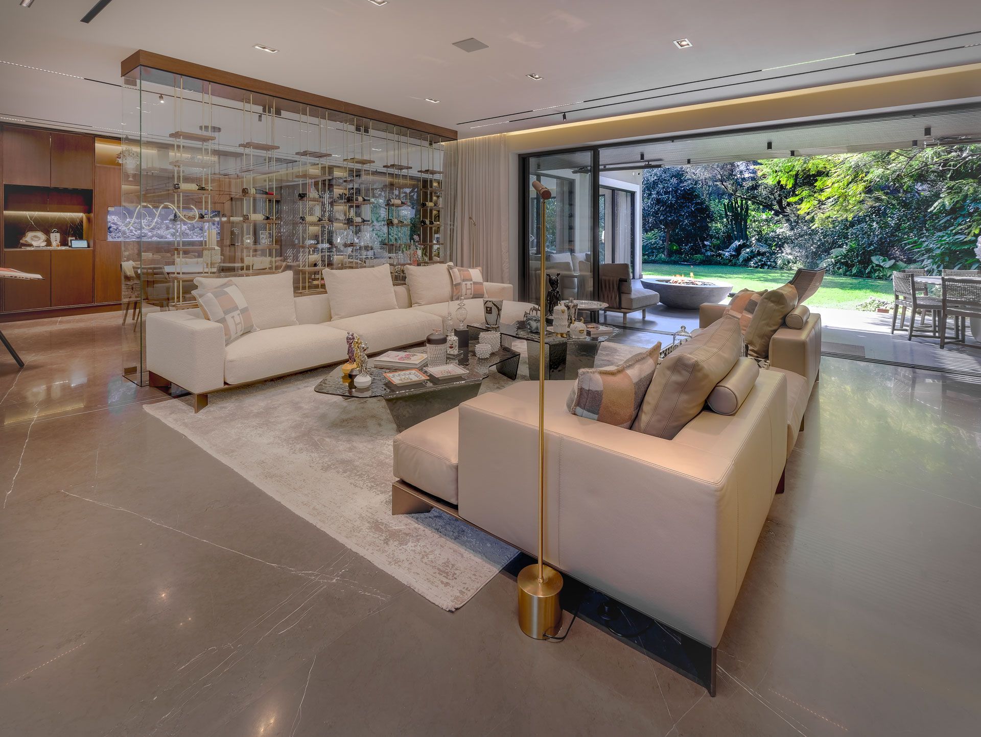 Salón moderno con sofás blancos, mampara de cristal, suelos pulidos y vistas a una exuberante vegetación exterior.