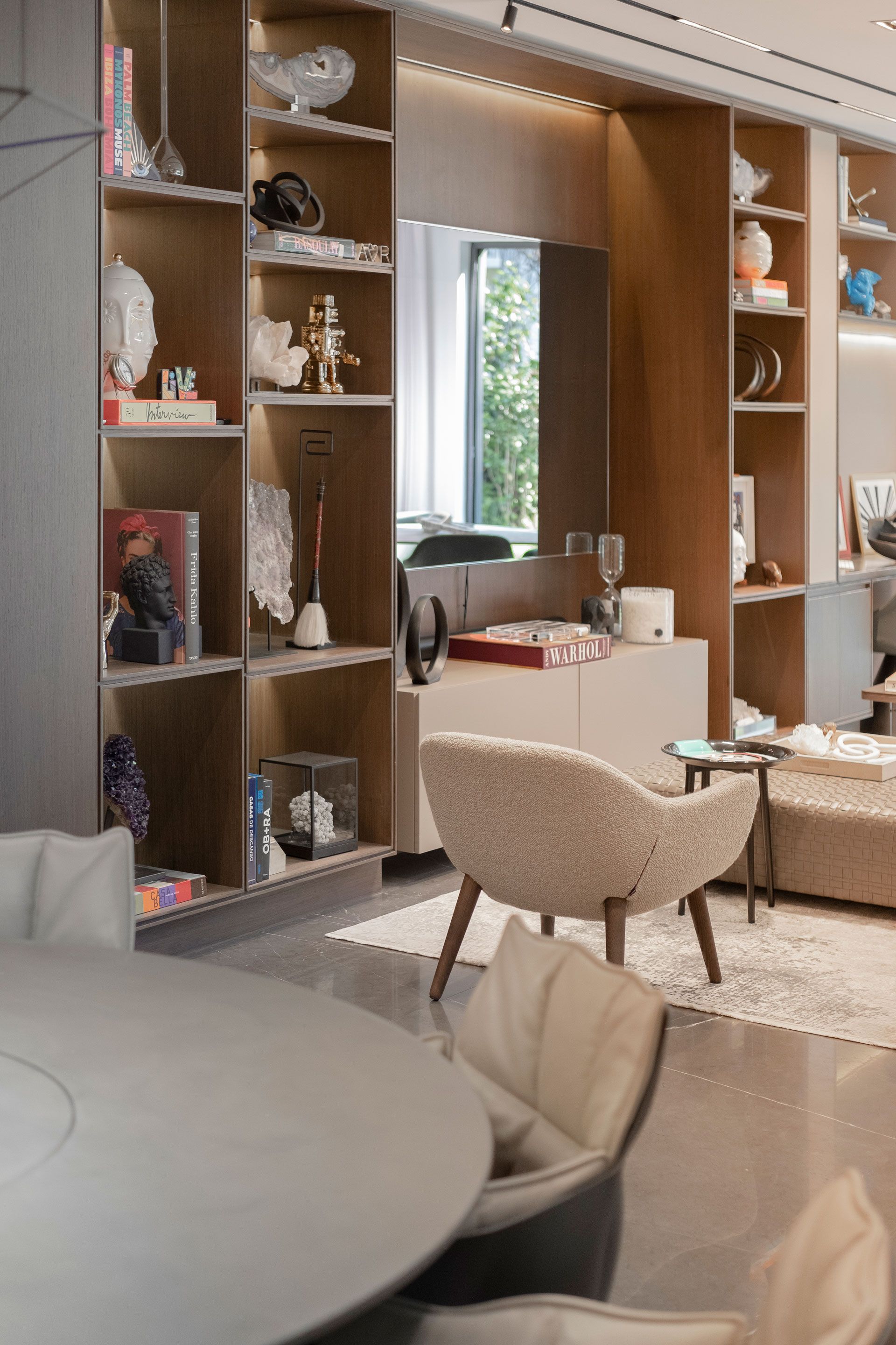 Sala de estar moderna con estanterías empotradas, un espejo y sillas beige alrededor de una mesa.
