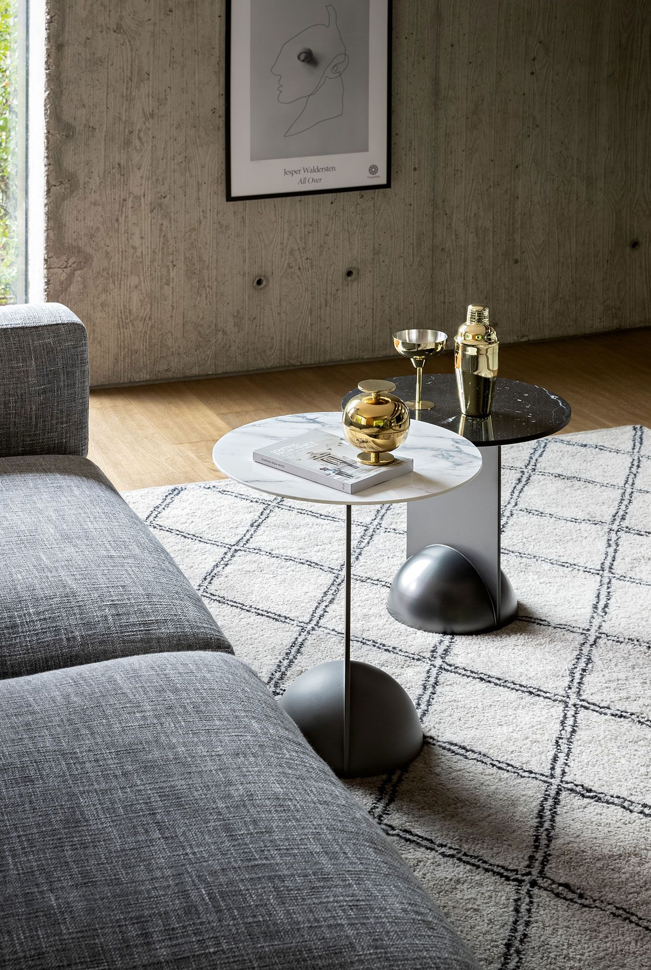 Sala de estar moderna con sofá gris, alfombra blanca y dos mesitas auxiliares con elementos decorativos.