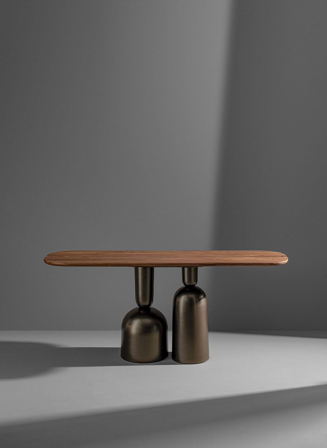 Banco bajo de madera con dos bases de pedestal de metal oscuro sobre un suelo de estudio gris.
