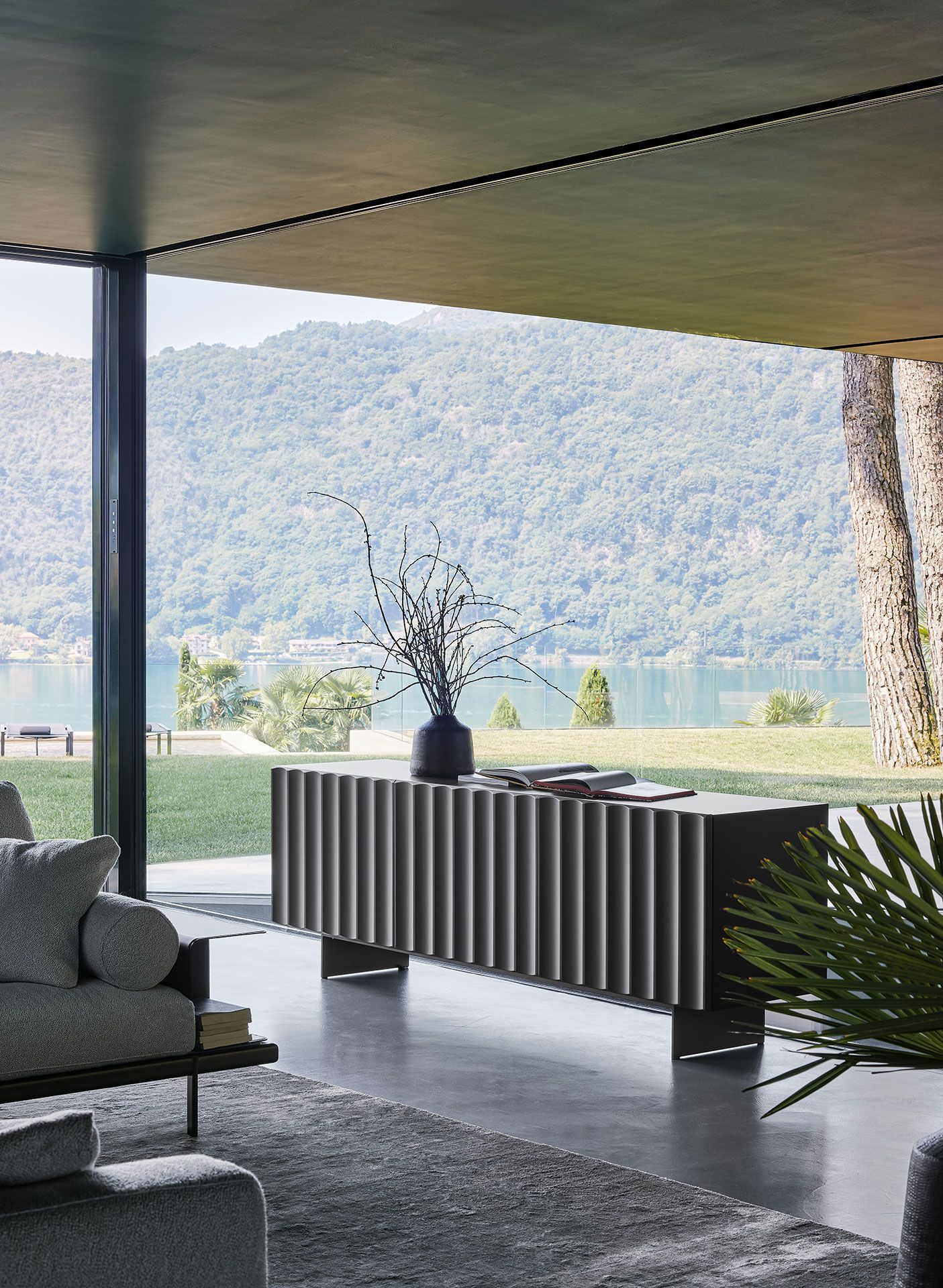Salón moderno con aparador a rayas, jarrón y vistas al lago de montaña a través de una gran ventana.
