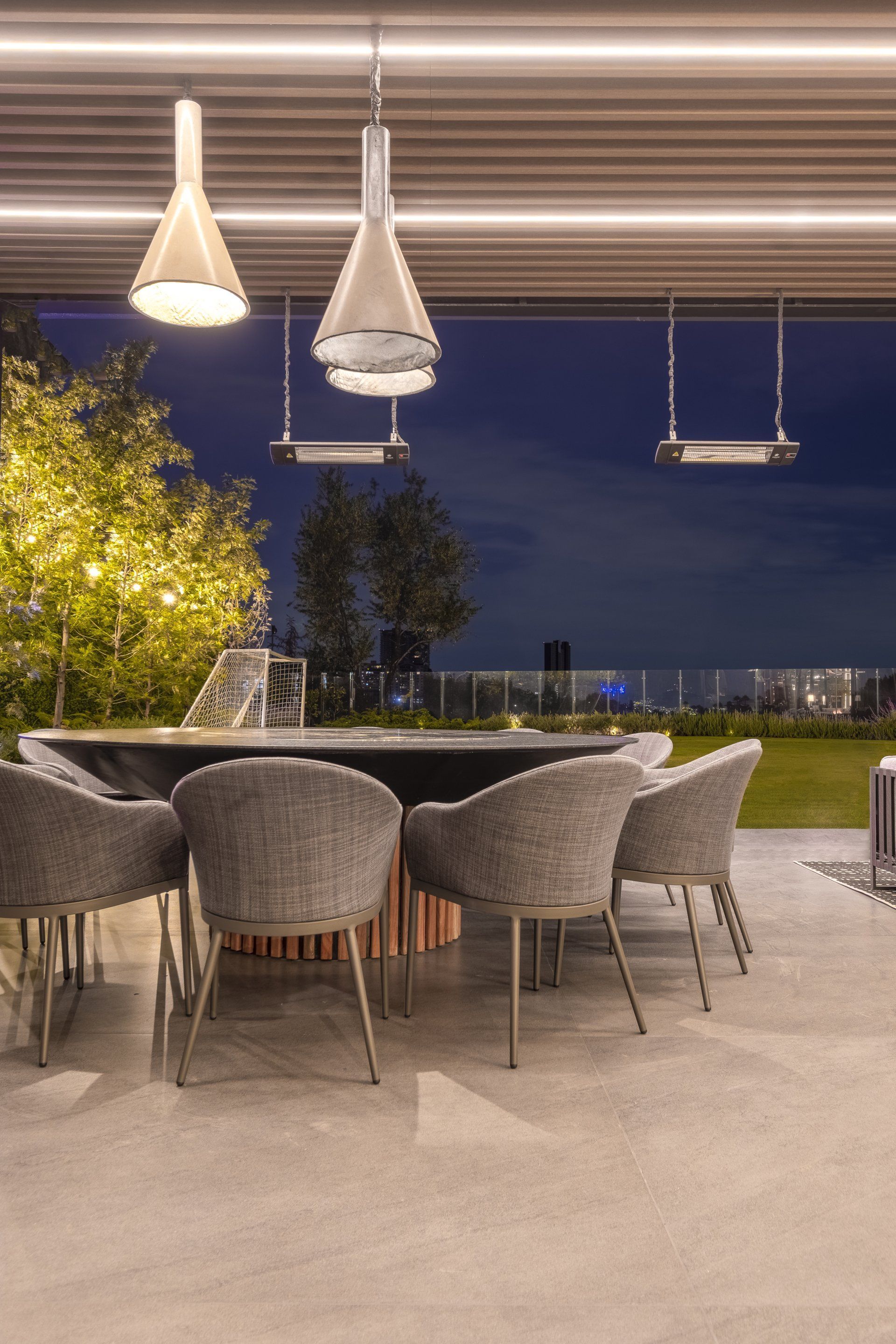 Comedor al aire libre en la terraza al atardecer con lámparas colgantes, mesas redondas y sillas de mimbre.