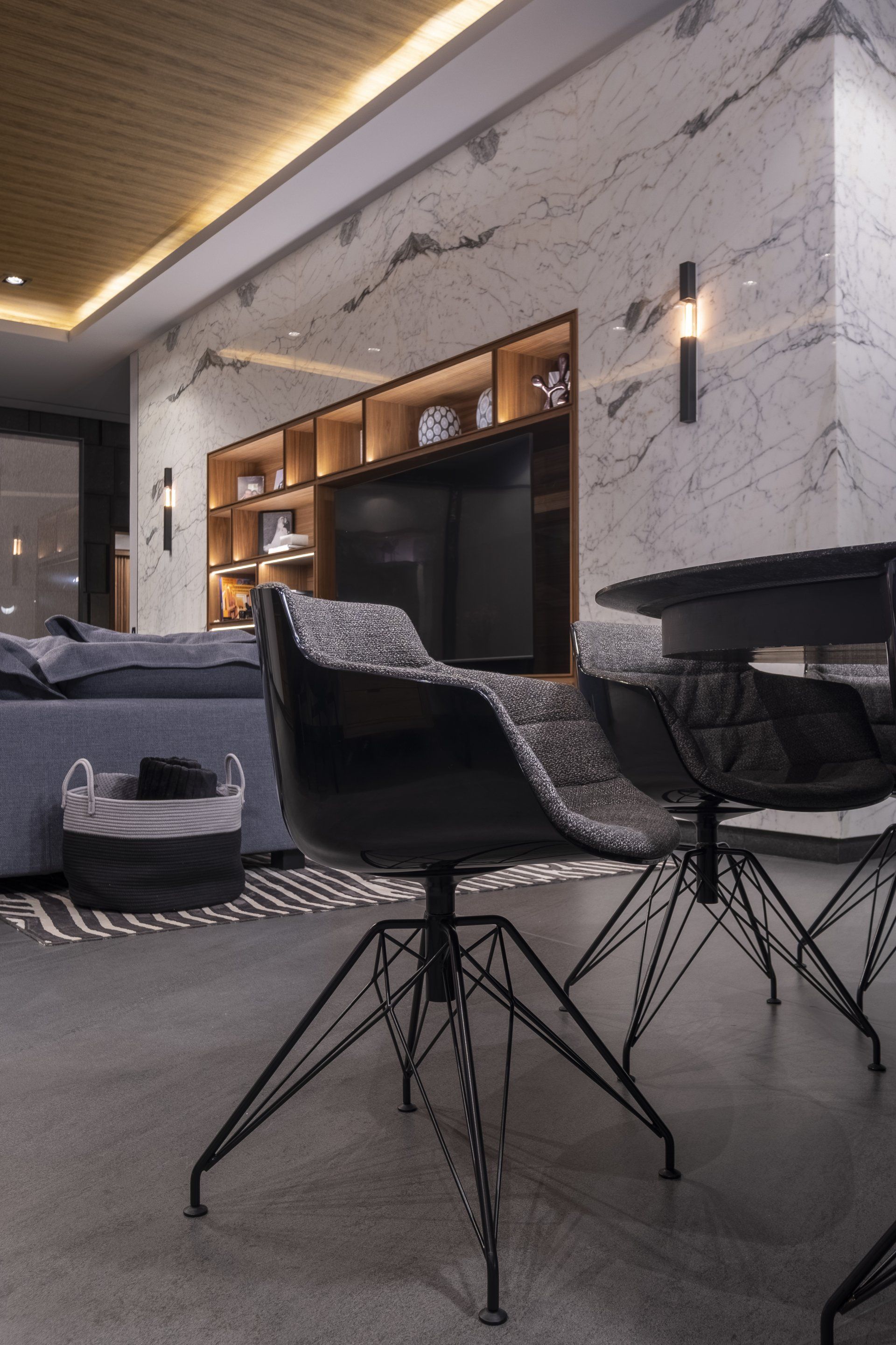 Sala de estar moderna con sillas negras, mesa redonda, sofá gris y mueble de pared de madera para la televisión.
