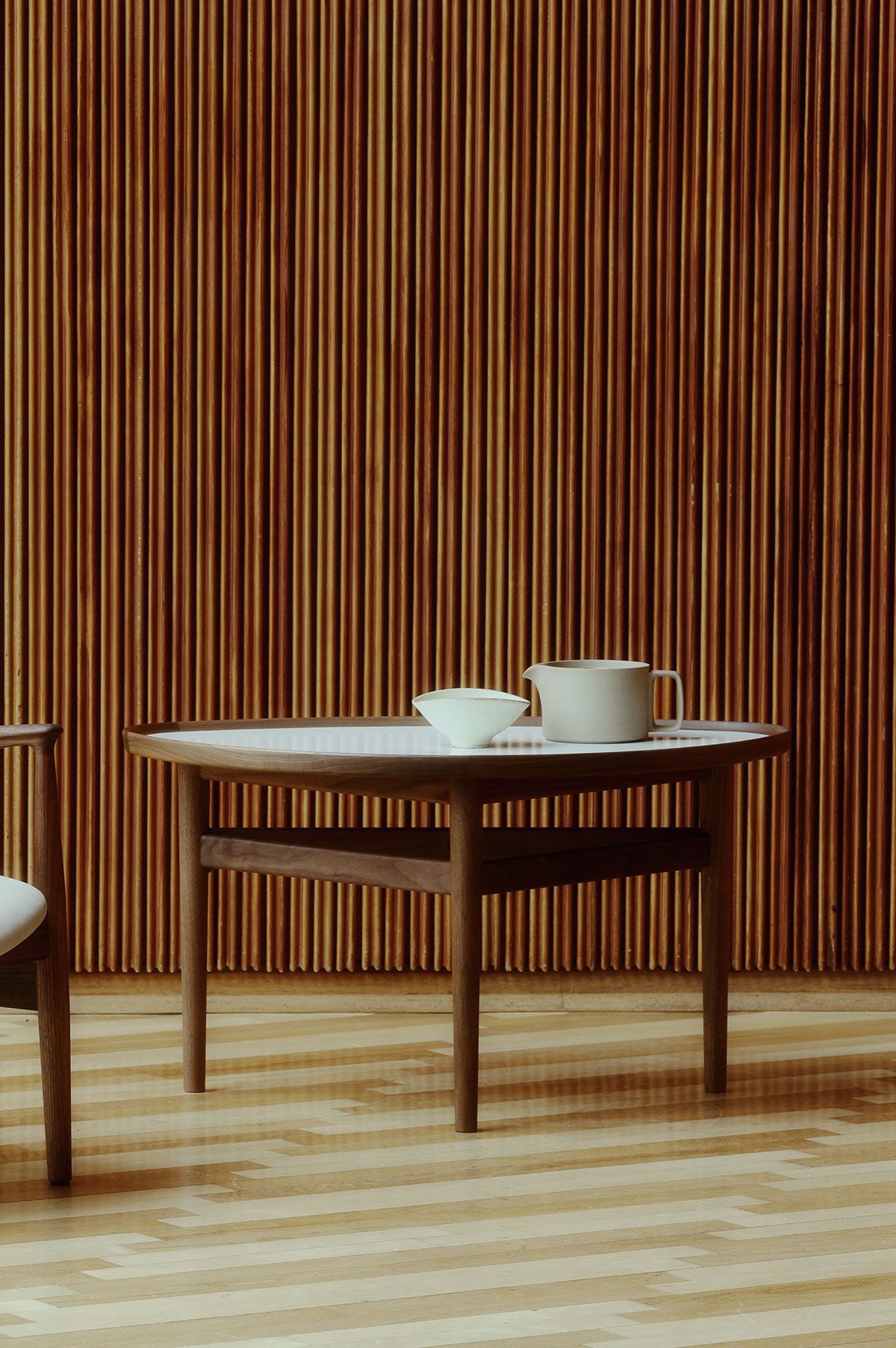 Mesa minimalista con una tetera y una taza blancas contra una pared de listones de madera.