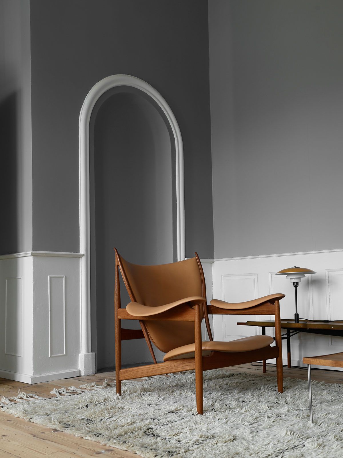 Sillón de cuero color canela en una habitación gris con una puerta arqueada y revestimiento de madera blanca.