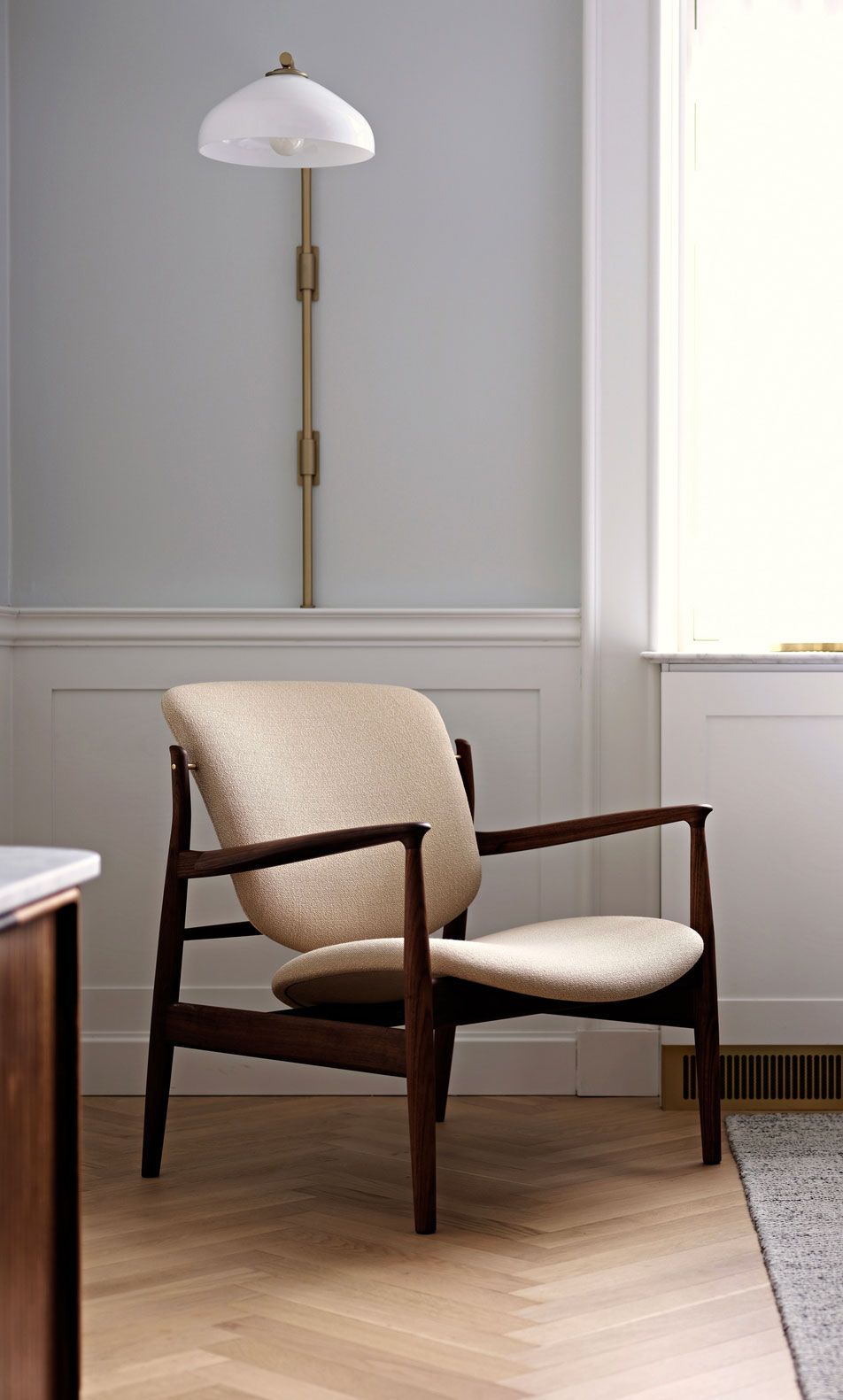 Sillón moderno con cojín beige en una habitación luminosa junto a una lámpara de pie.