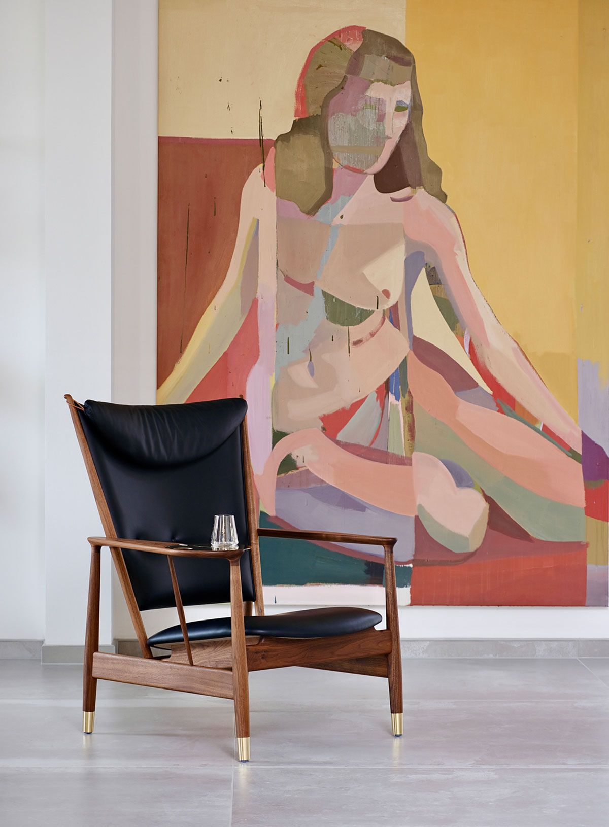 Sillón de cuero negro frente a un gran cuadro abstracto en una habitación luminosa.