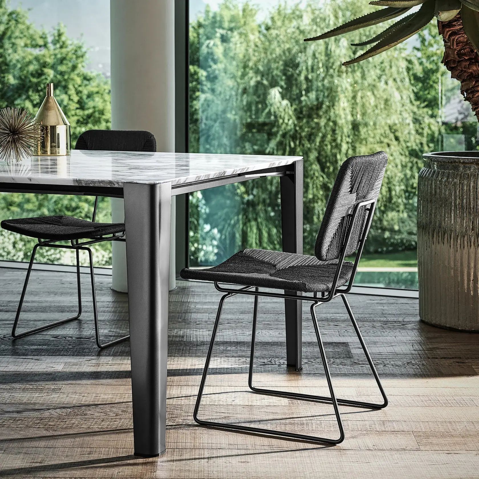 Conjunto de comedor moderno para patio con sillas oscuras y una mesa con vistas a un jardín exuberante.