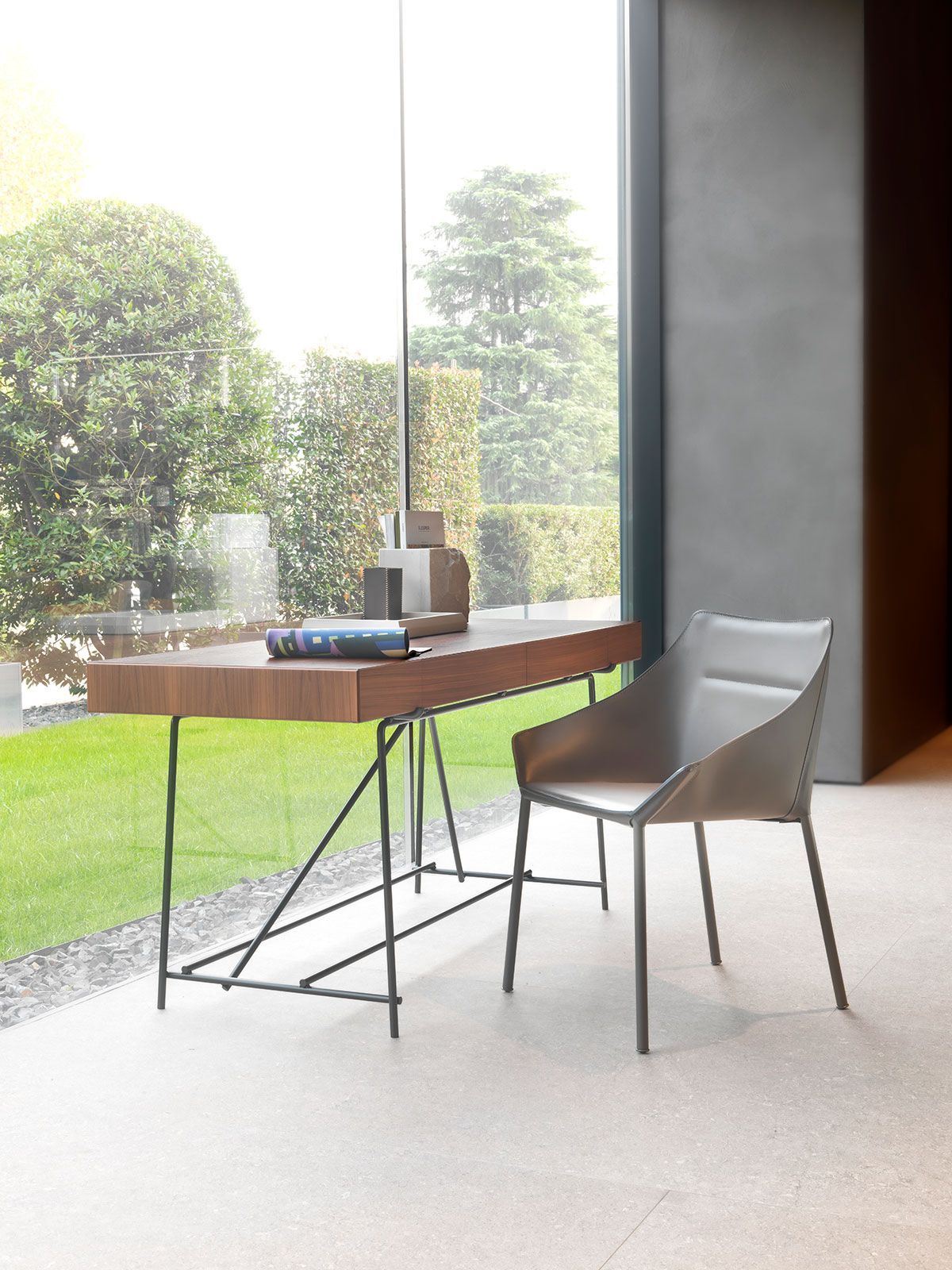 Escritorio moderno junto a una gran ventana con una silla blanca y vistas al jardín.
