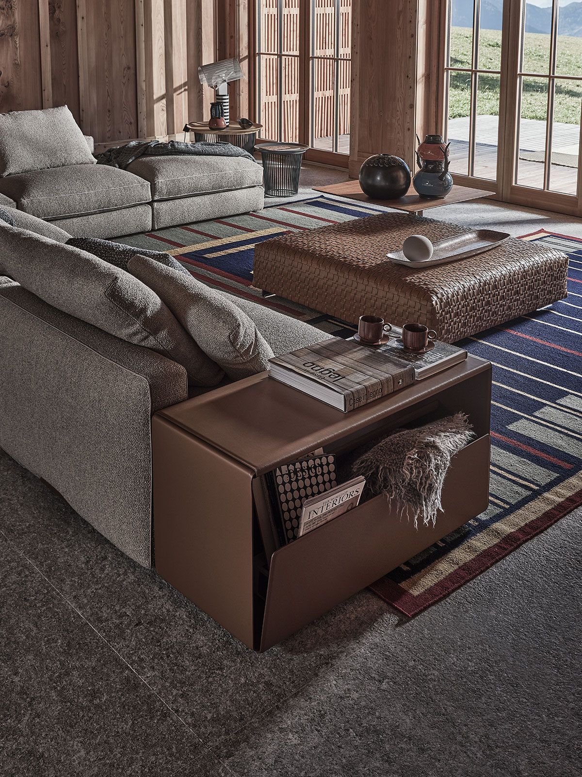 Sala de estar con sofá modular, mesa de centro de madera y alfombra estampada junto a grandes ventanales.