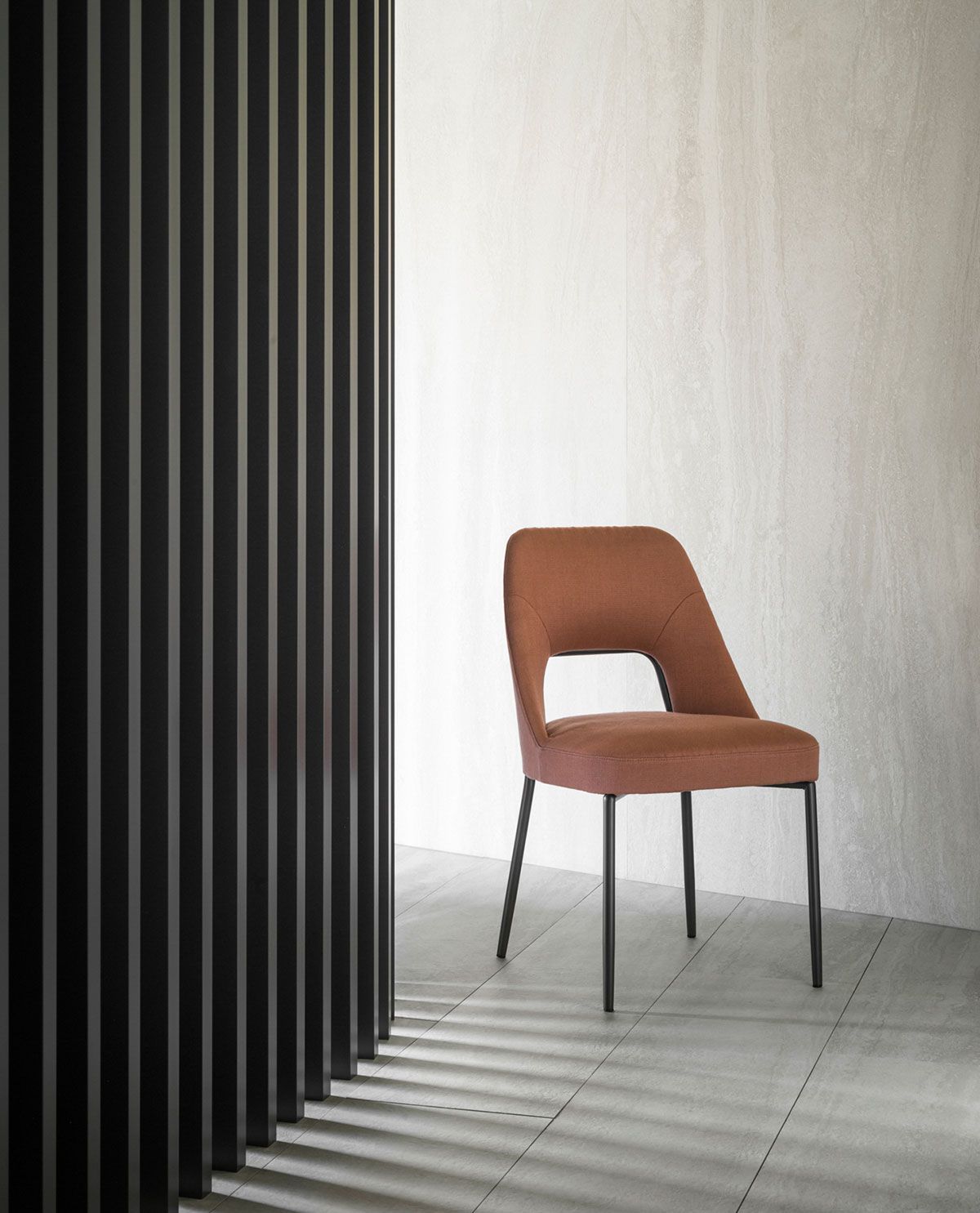 Silla marrón en una habitación minimalista junto a una pared de listones negros y una pared blanca texturizada.