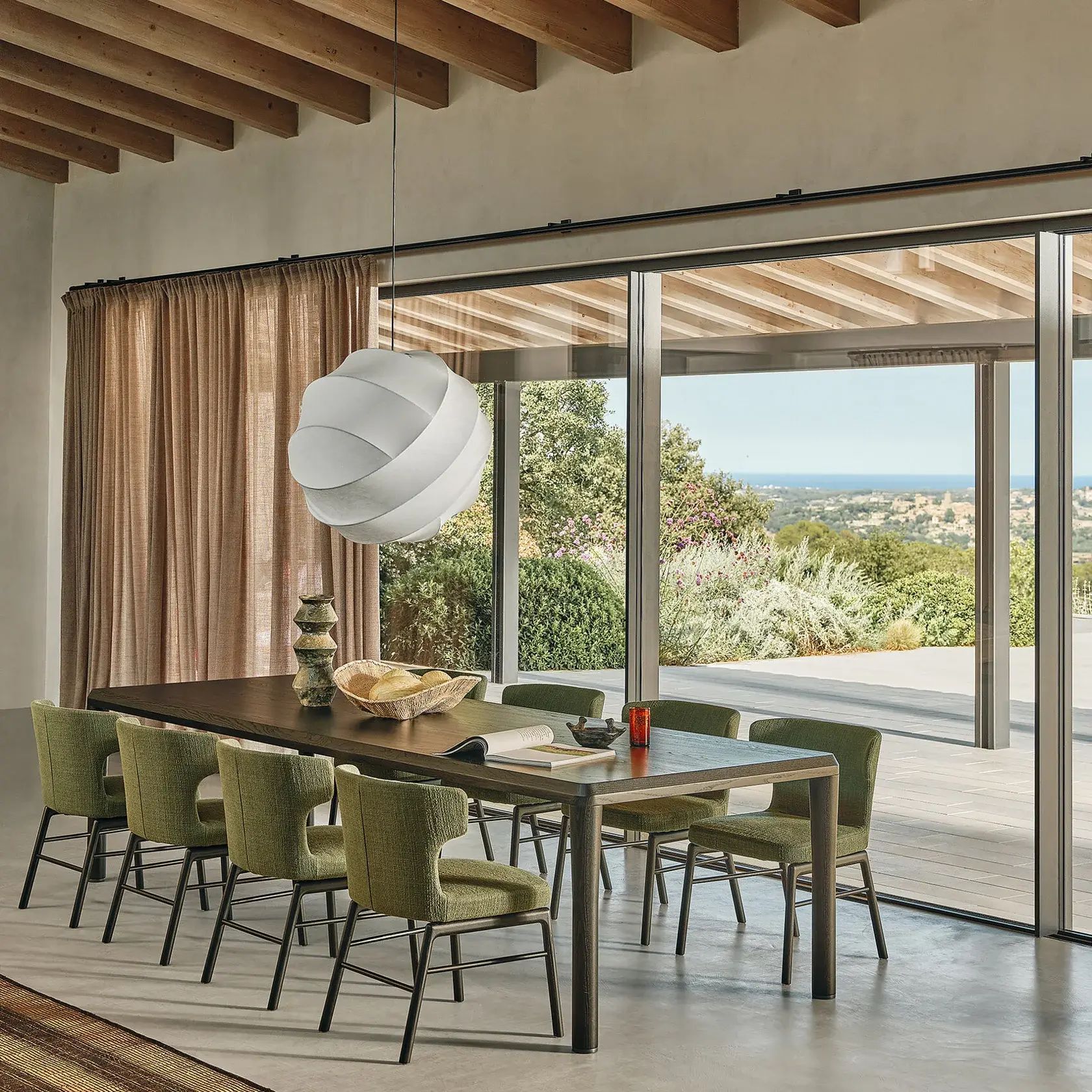 Comedor moderno con sillas verdes, mesa de madera y grandes puertas correderas que dan a un patio con vistas al mar.