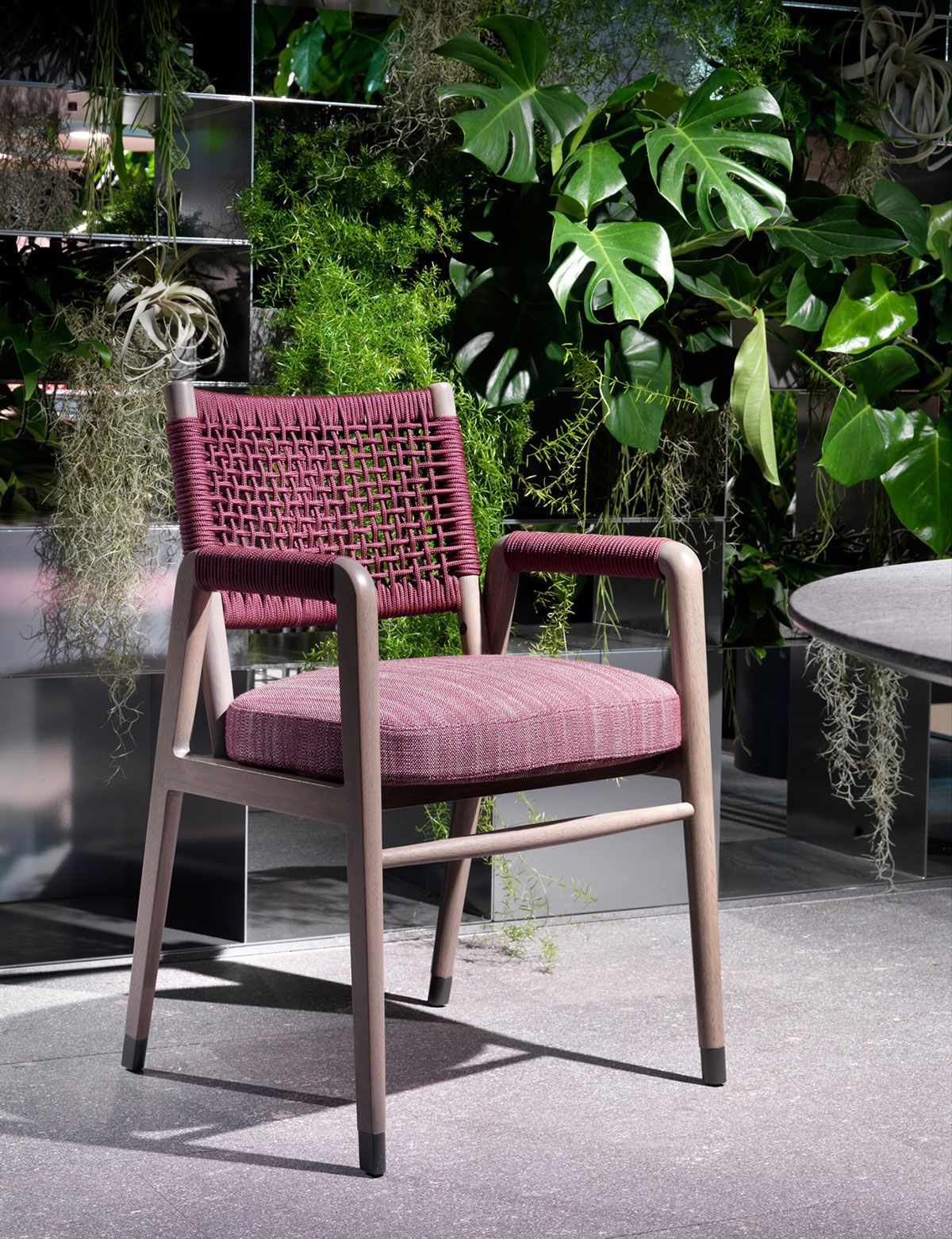Silla rosa tejida en un patio junto a exuberantes plantas verdes y una mesa redonda.