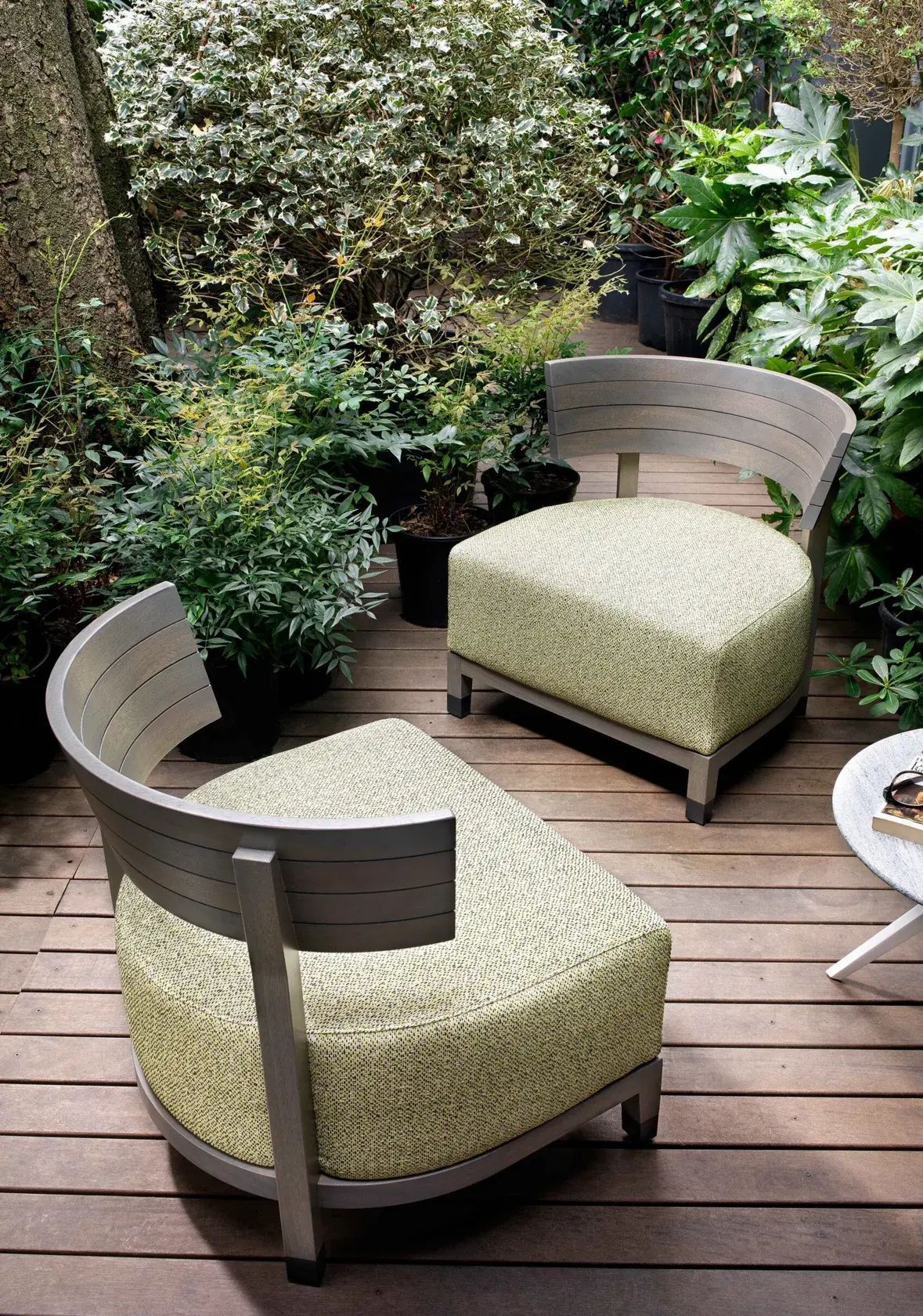 Dos sillas de madera acolchadas en una terraza en un entorno de jardín exuberante.