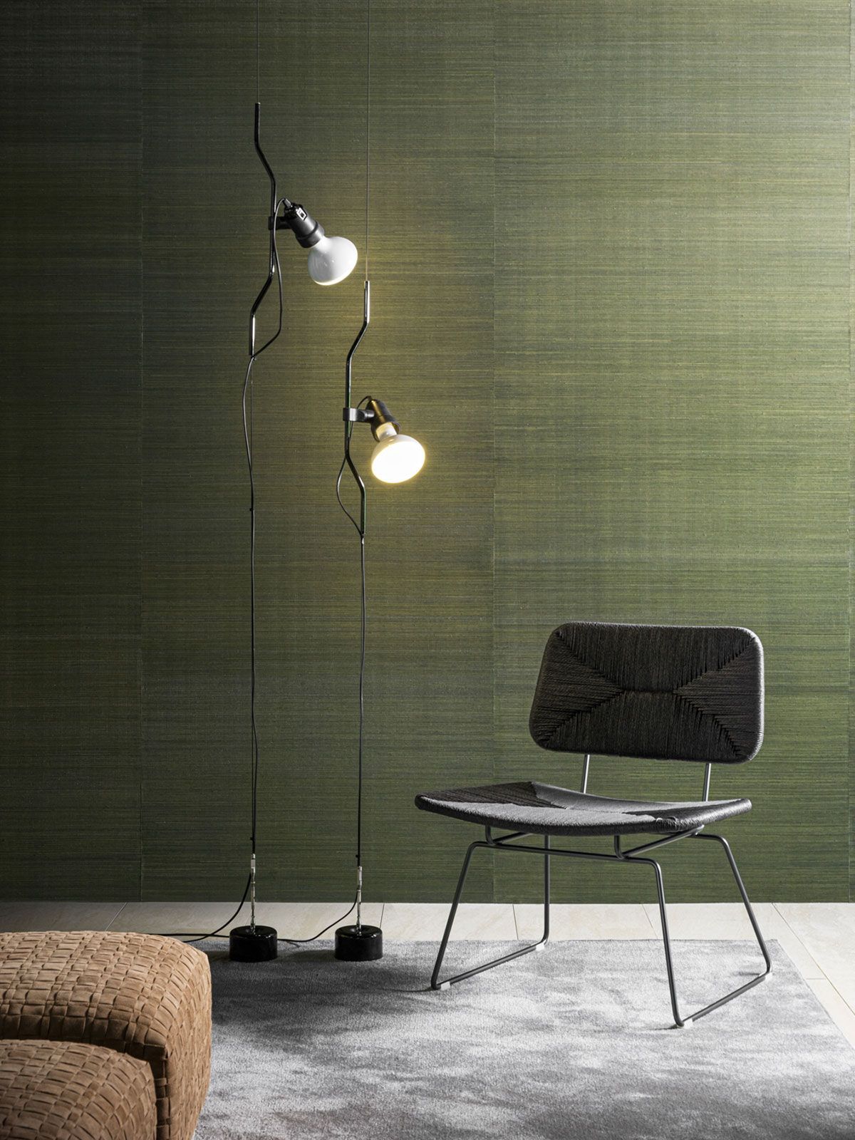 Silla moderna y dos lámparas de pie contra una pared verde texturizada en una habitación minimalista.