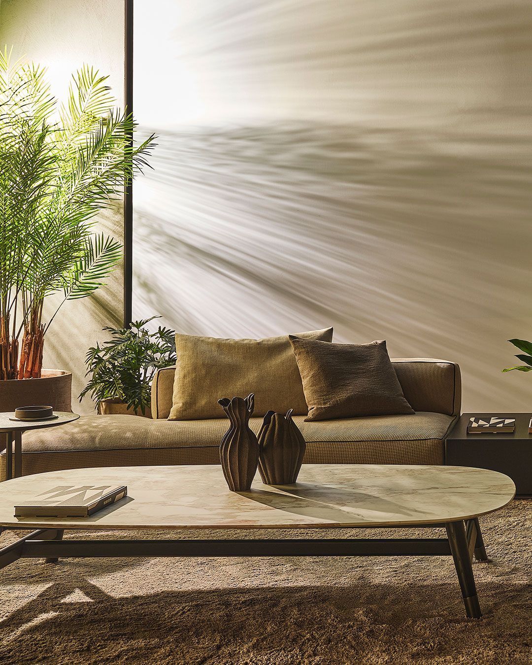 Sunlit modern living room with beige sofa, plants, and a low coffee table against a textured wall.