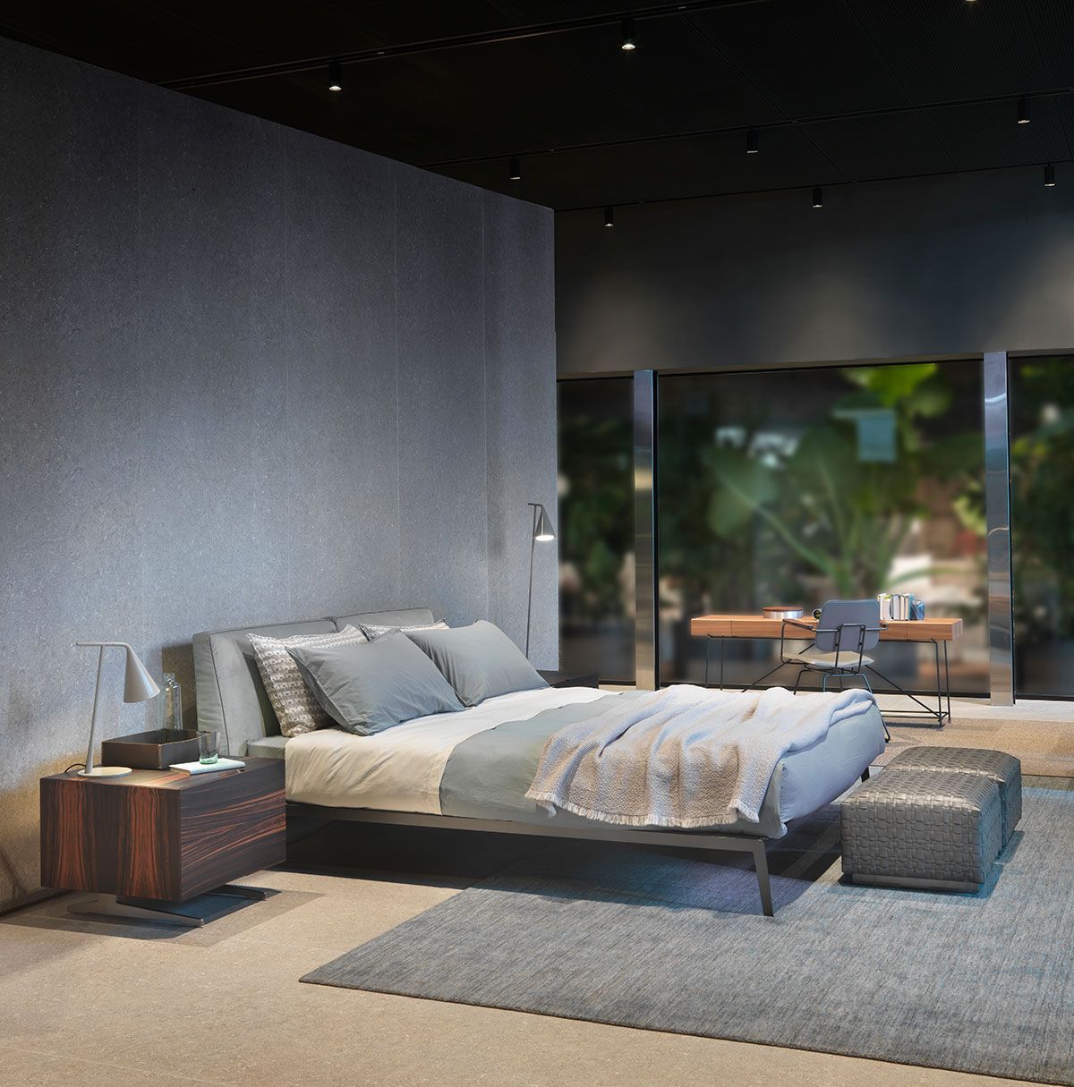 Dormitorio moderno con cama gris, mesita de noche de madera y una gran pared de cristal con vistas a la vegetación.