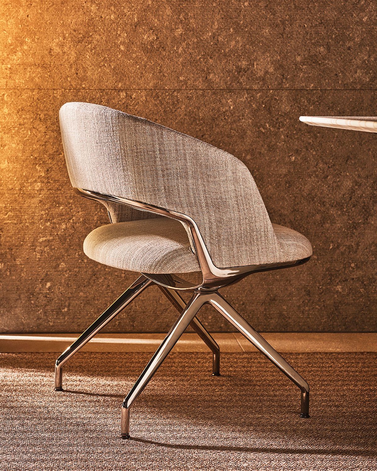 Silla moderna tapizada en gris con patas de metal sobre un fondo de pared texturizada marrón.