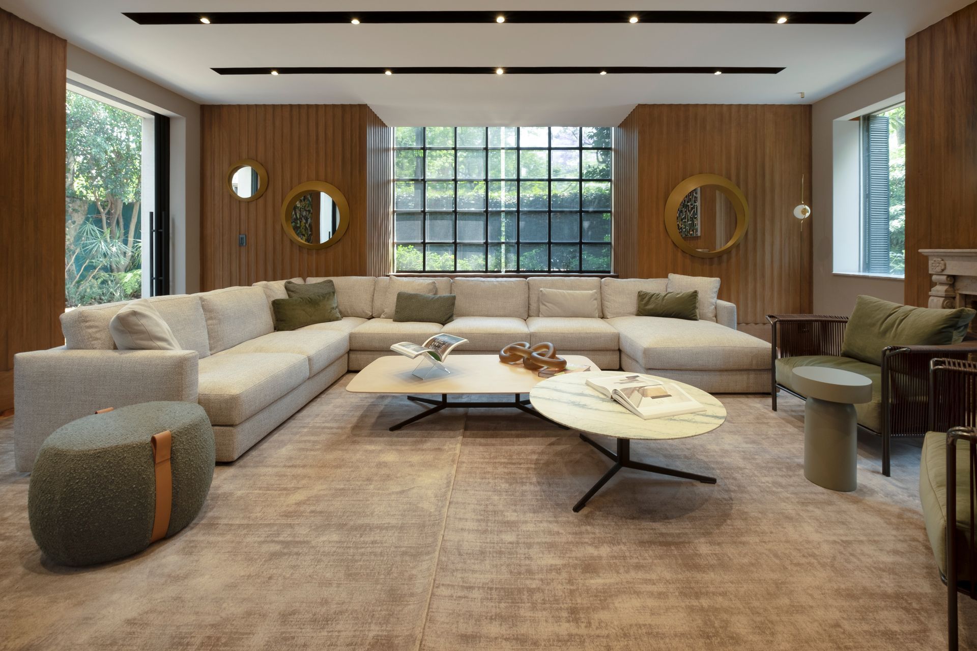 Sala de estar moderna con sofá seccional beige, mesas de centro redondas, paredes revestidas de madera y grandes ventanales.