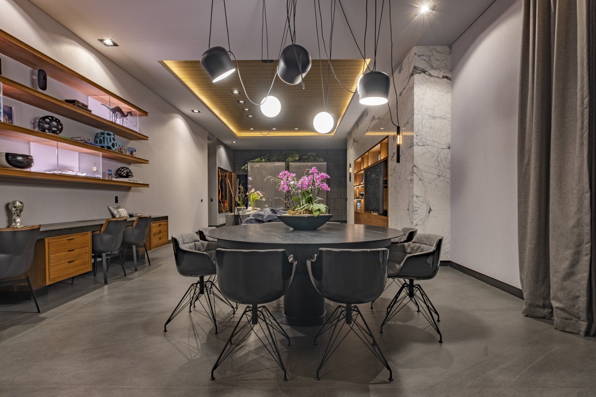 Comedor moderno con sillas negras, una mesa redonda, lámparas colgantes y un arreglo floral en el centro.