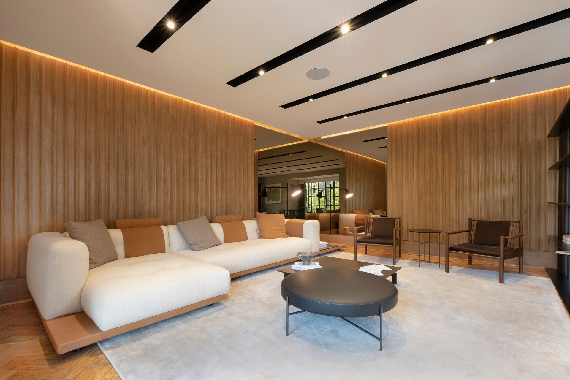 Salón moderno con sofá blanco curvo, mesa de centro redonda, paredes revestidas de madera y luces empotradas en el techo.