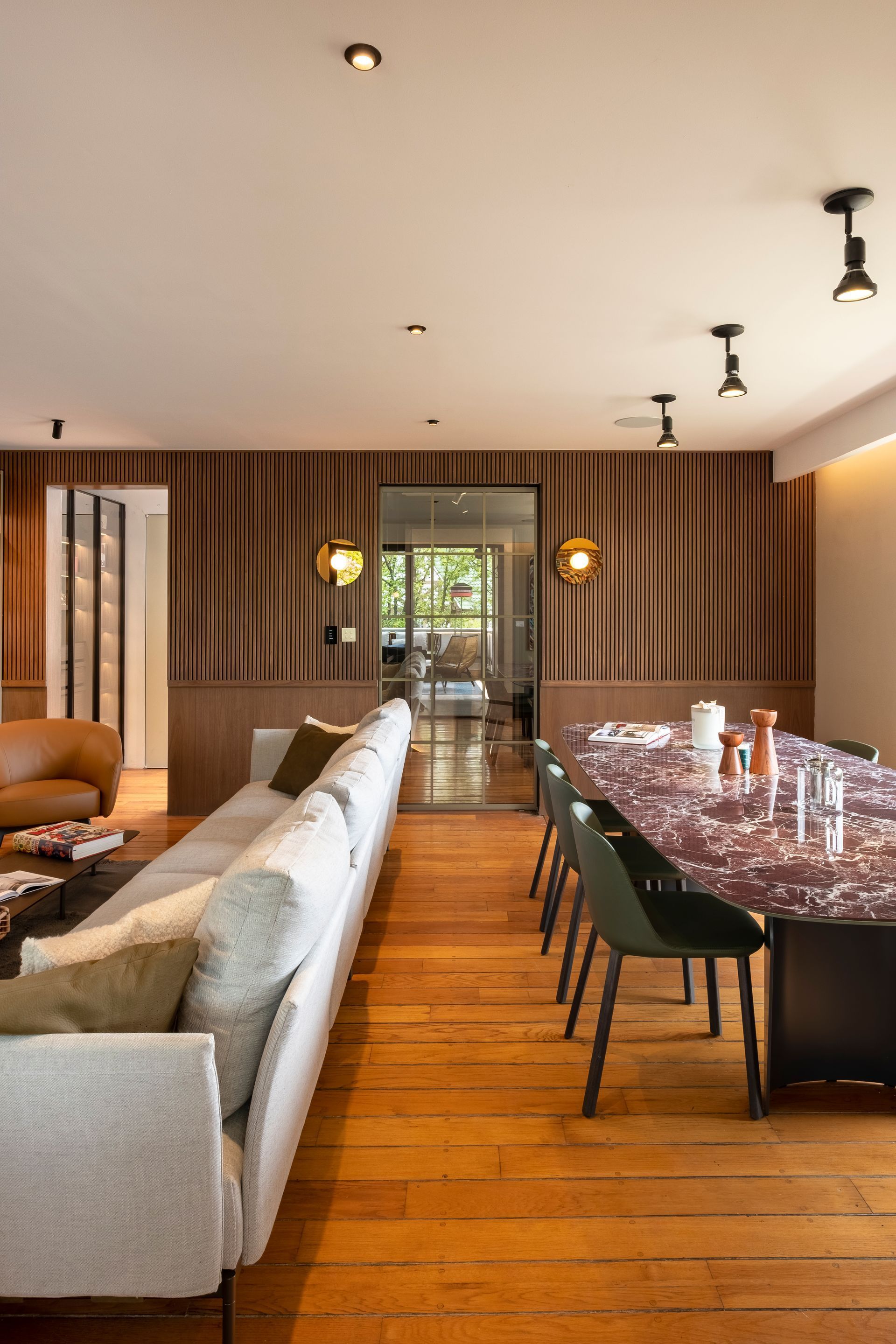 Comedor moderno con suelo de madera, pared a rayas, sofá y mesa larga con sillas.