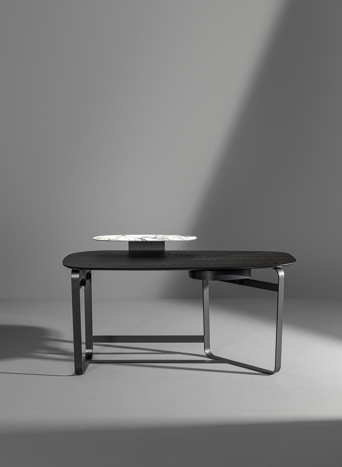 Mesa pequeña negra con un libro o caja encima, sobre un fondo de estudio gris liso.
