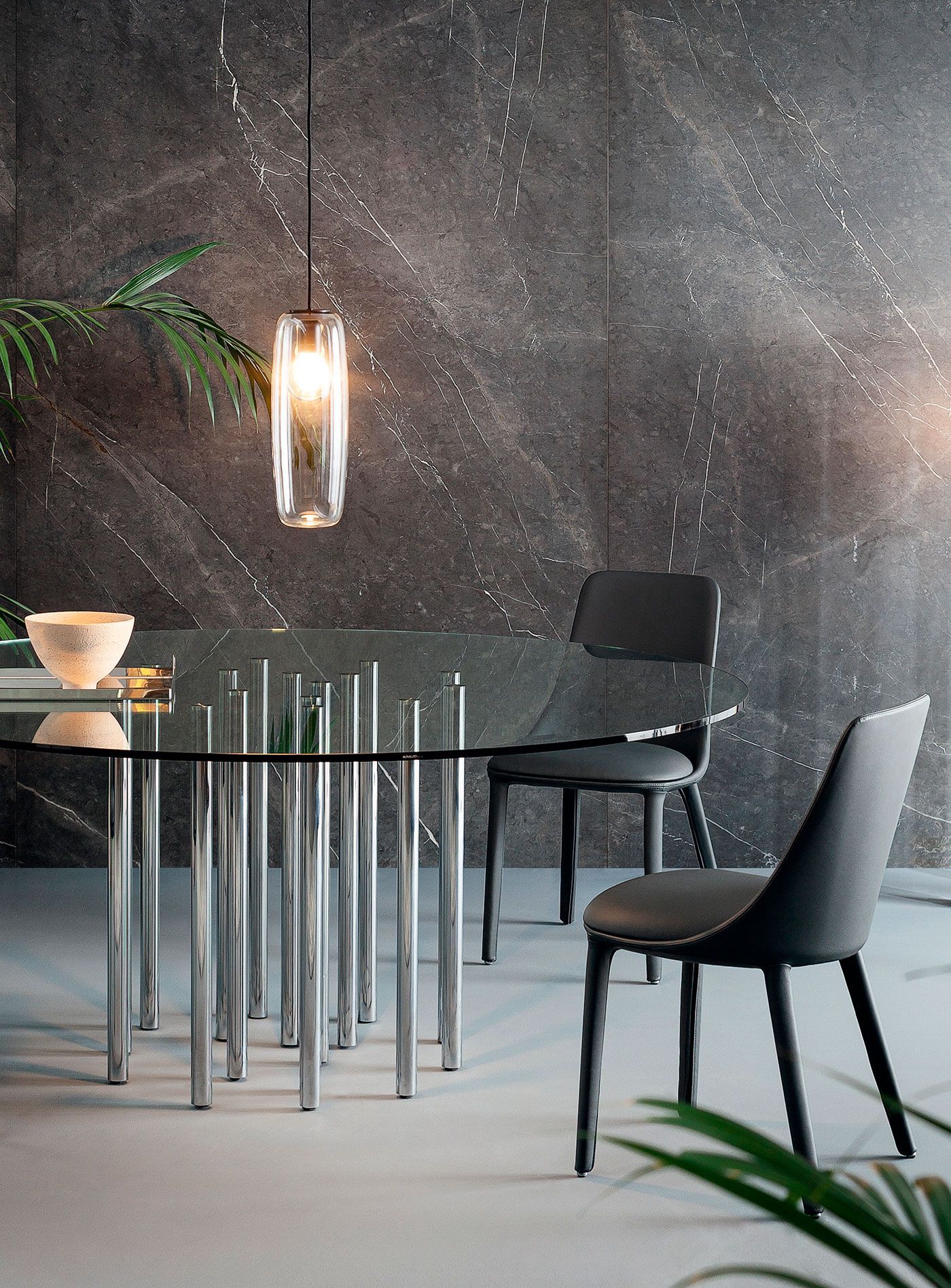 Comedor moderno con mesa de cristal, sillas negras y lámpara colgante sobre una pared oscura texturizada.