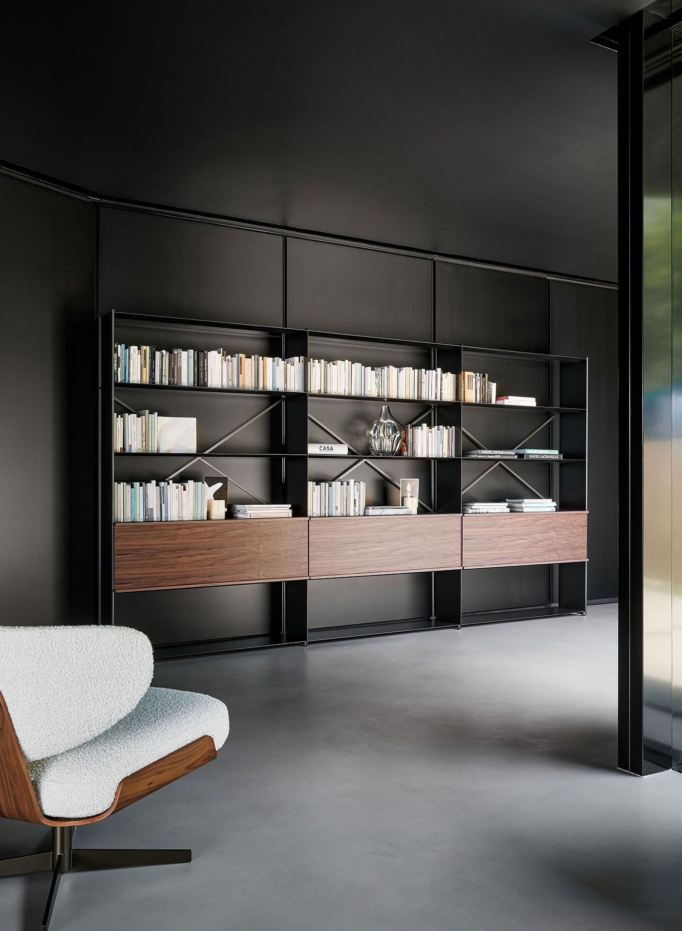 Sala de estar moderna con estanterías empotradas oscuras, libros y un sofá gris claro.
