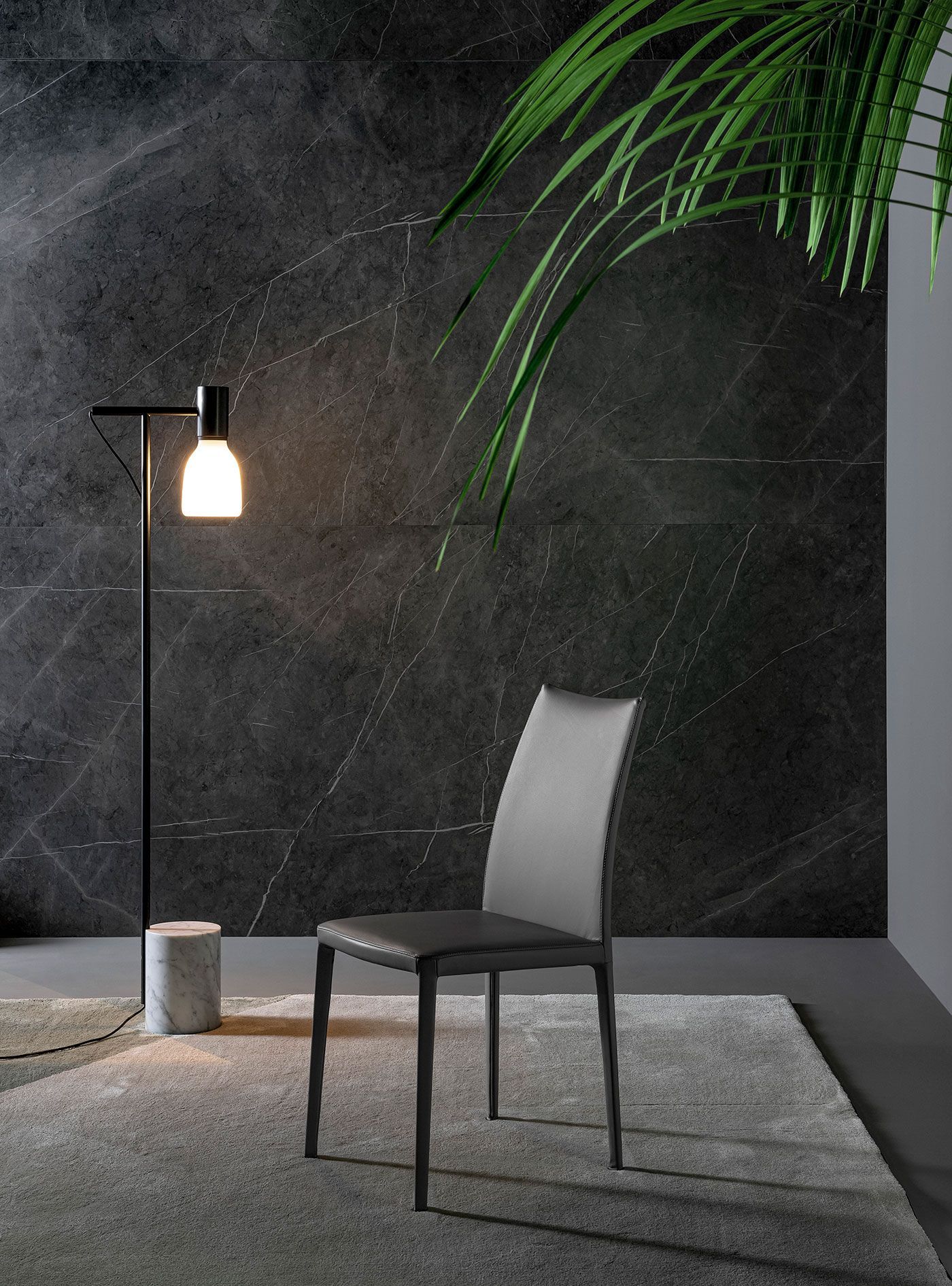 Silla moderna junto a una lámpara de pie encendida sobre una alfombra en una habitación oscura y minimalista