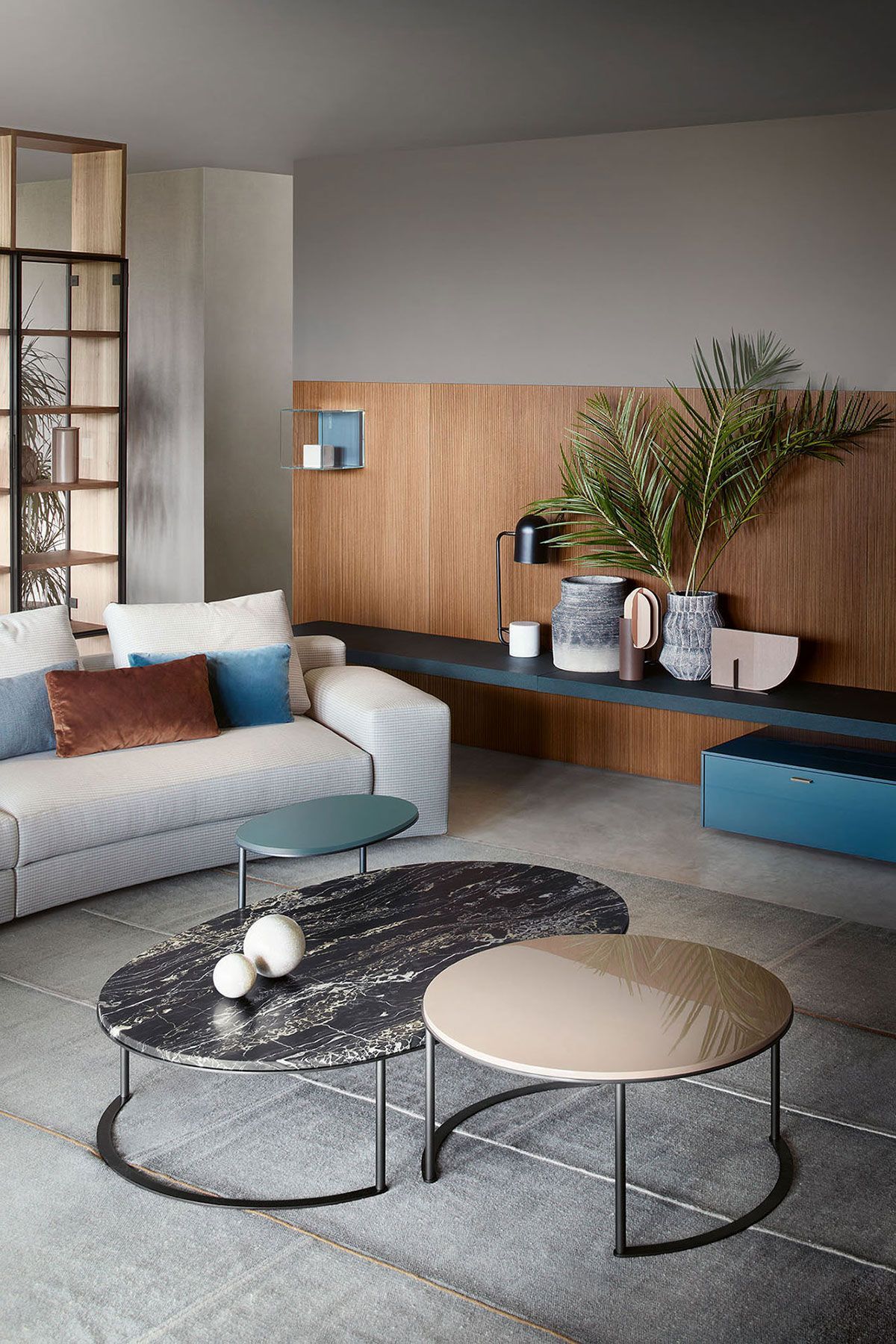 Sala de estar moderna con sofá blanco, pared revestida de madera, banco azul y mesas de centro redondas.
