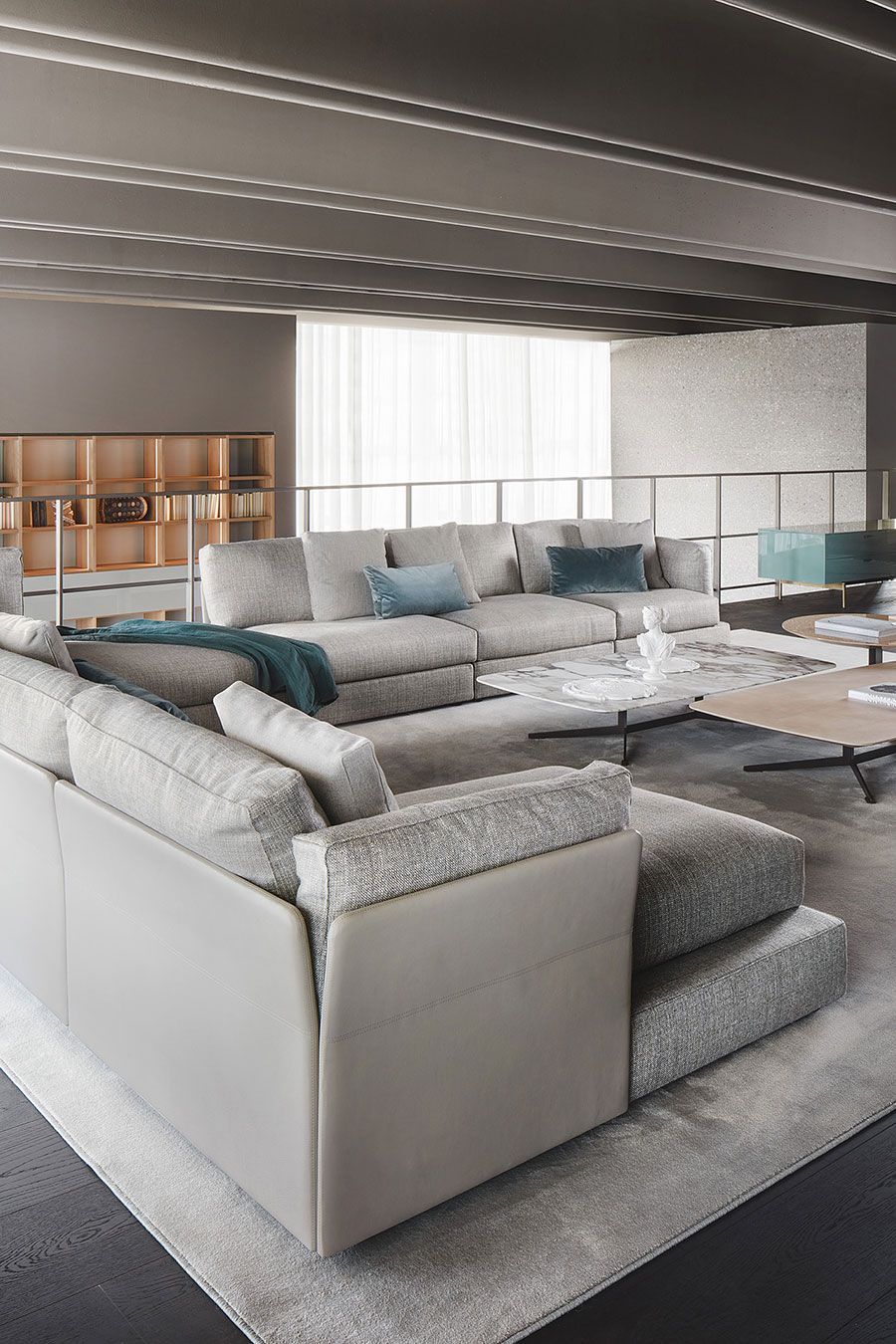 Salón moderno de planta abierta con grandes sofás seccionales blancos, cojines azules y vistas al mar.