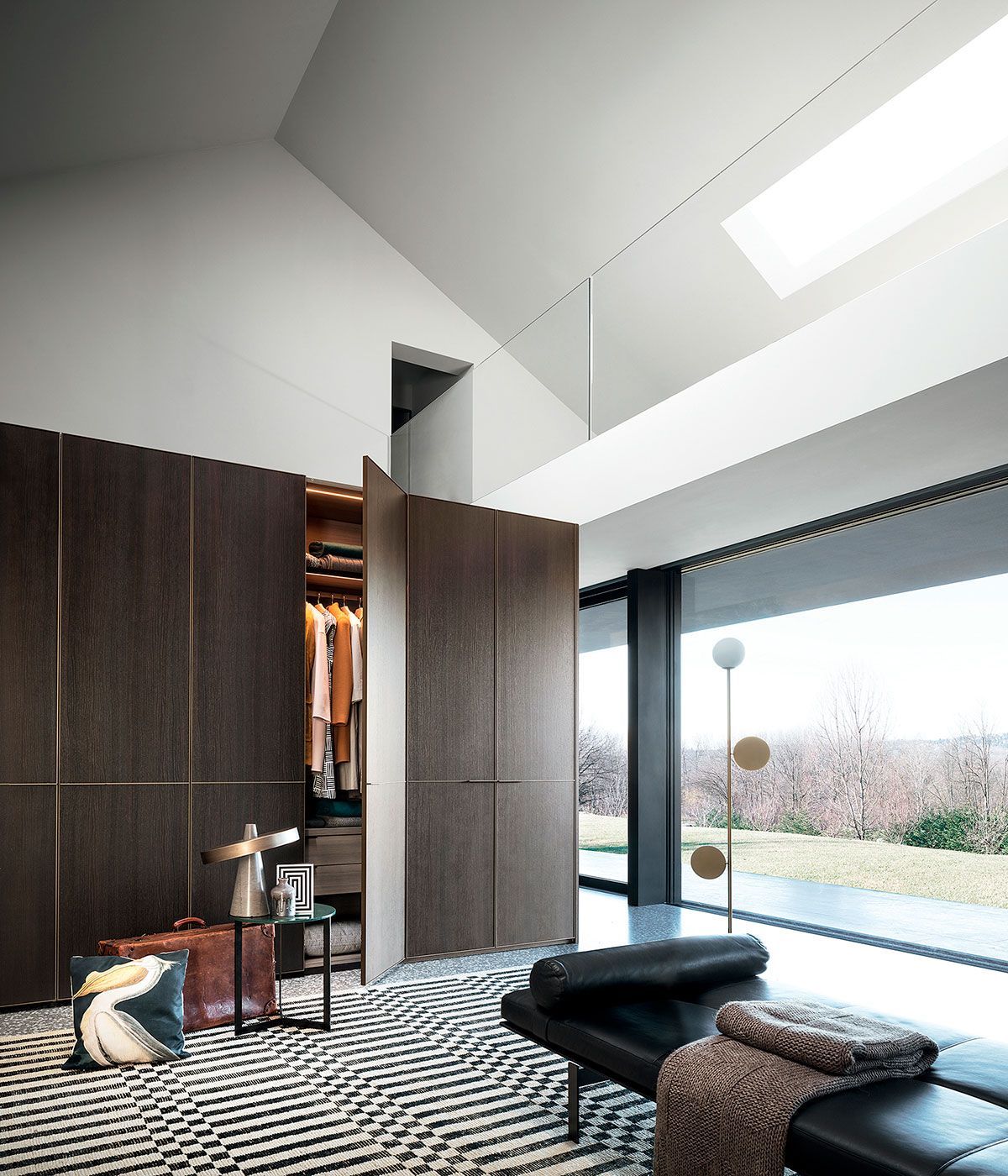 Salón moderno con paredes de madera oscura, alfombra estampada, sofá negro y grandes puertas de cristal que dan a un jardín.