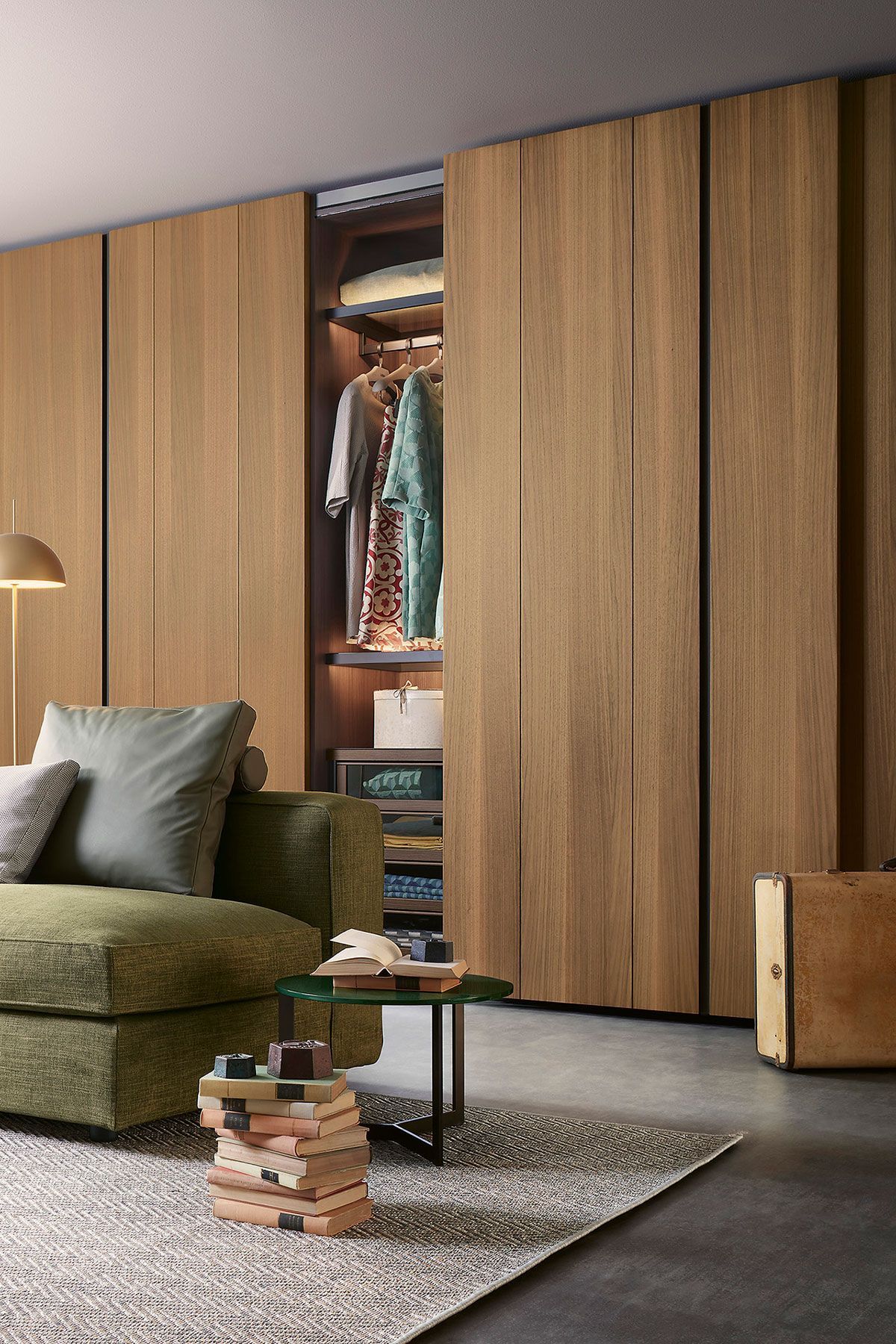 Sala de estar moderna con puertas de armario de madera, sofá verde, alfombra y libros apilados sobre una mesa.