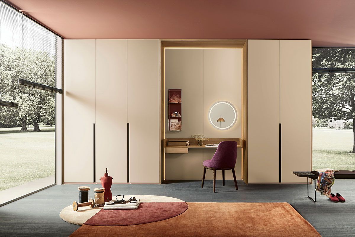 Dormitorio moderno con armarios beige, tocador central, silla morada y grandes ventanales.