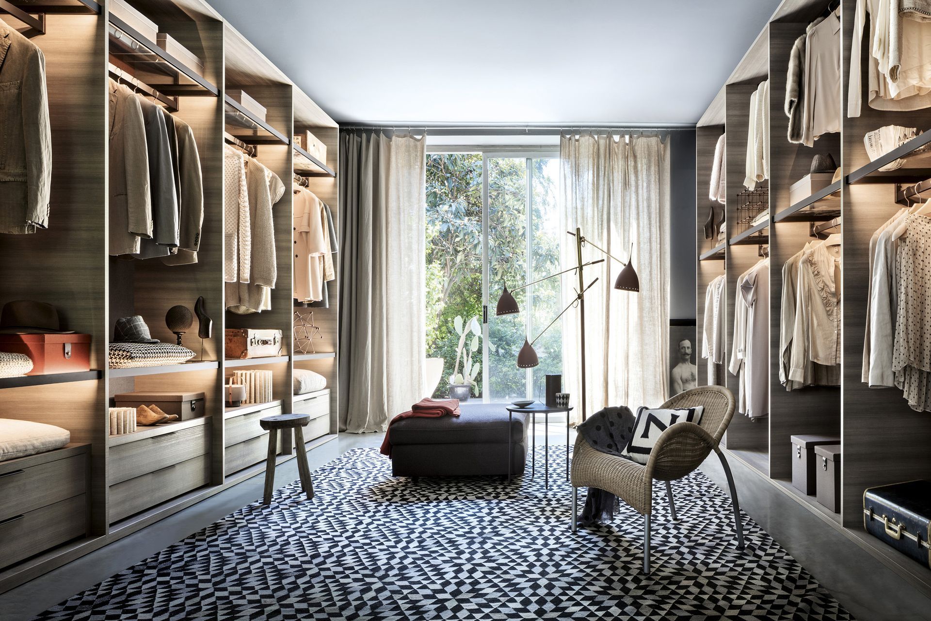Vestidor moderno con estantes, perchero, alfombra estampada, silla y rincón de lectura junto a la ventana.