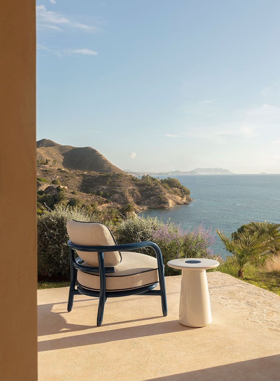 Silla de patio y mesa auxiliar con vistas a una soleada costa rocosa y al mar azul.
