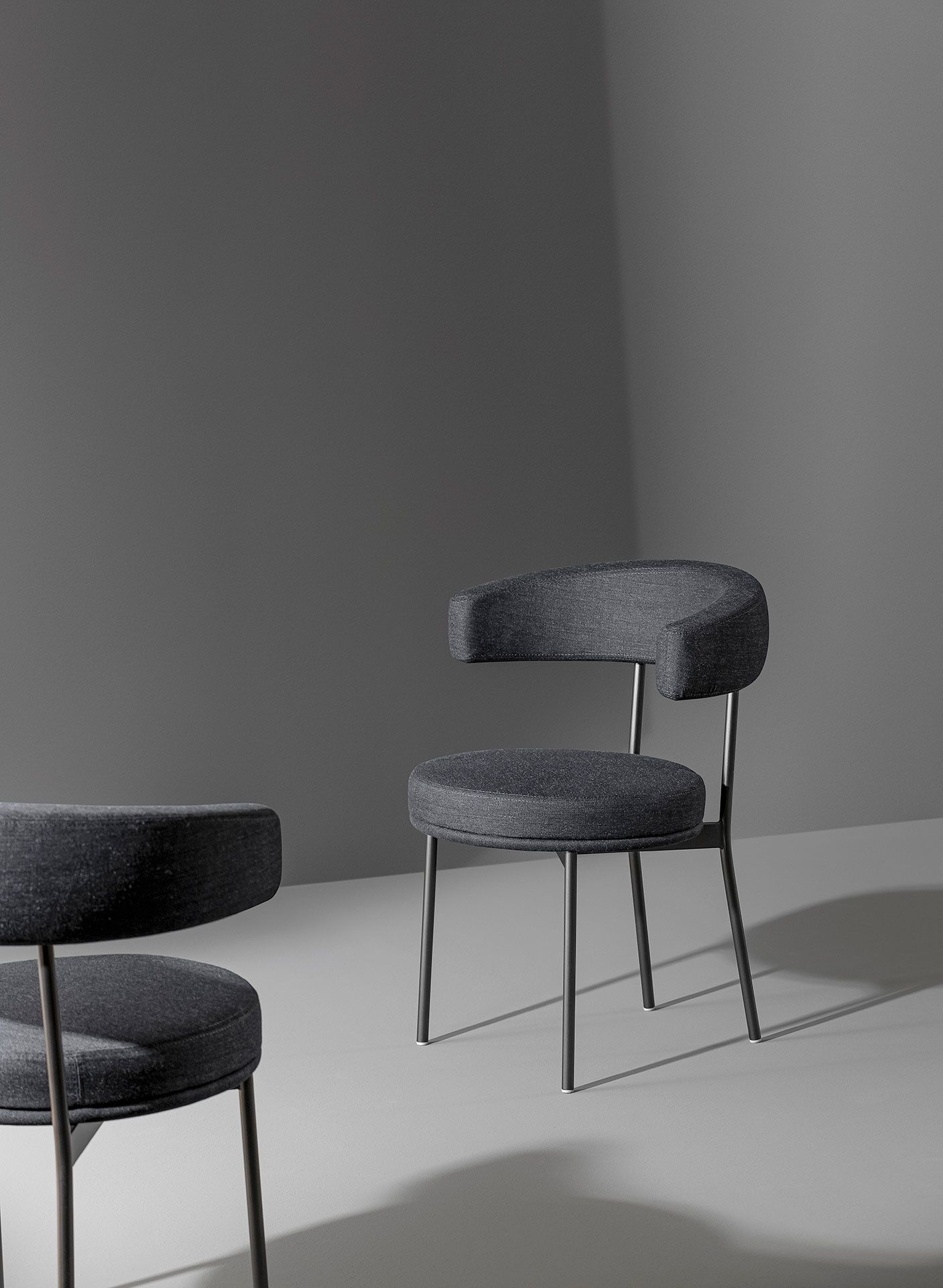 Dos sillas de color gris oscuro en una habitación minimalista gris, una en el centro y la otra parcialmente visible