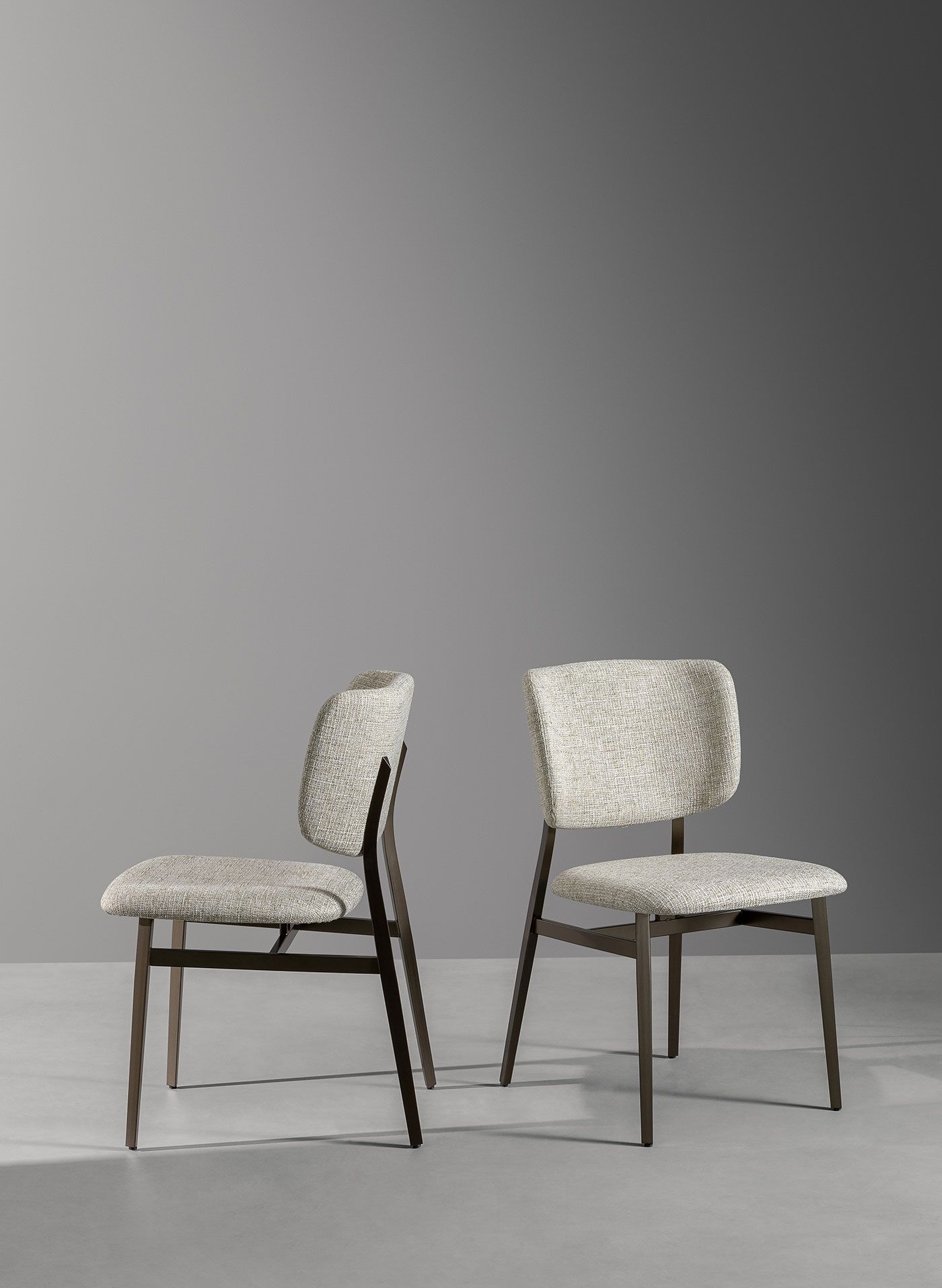 Dos sillas tapizadas de color beige, una frente a la otra, sobre un fondo de estudio gris.