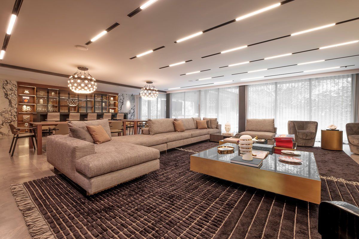 Sala de estar moderna con sofá seccional beige, mesa de centro de madera, alfombra estampada y grandes ventanales