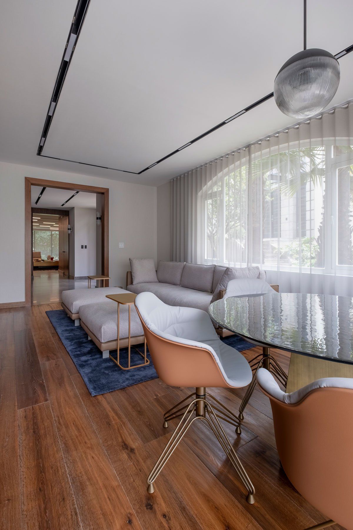 Sala de estar moderna con sofá gris, alfombra azul, mesa de centro de cristal y cortinas arqueadas en la ventana.